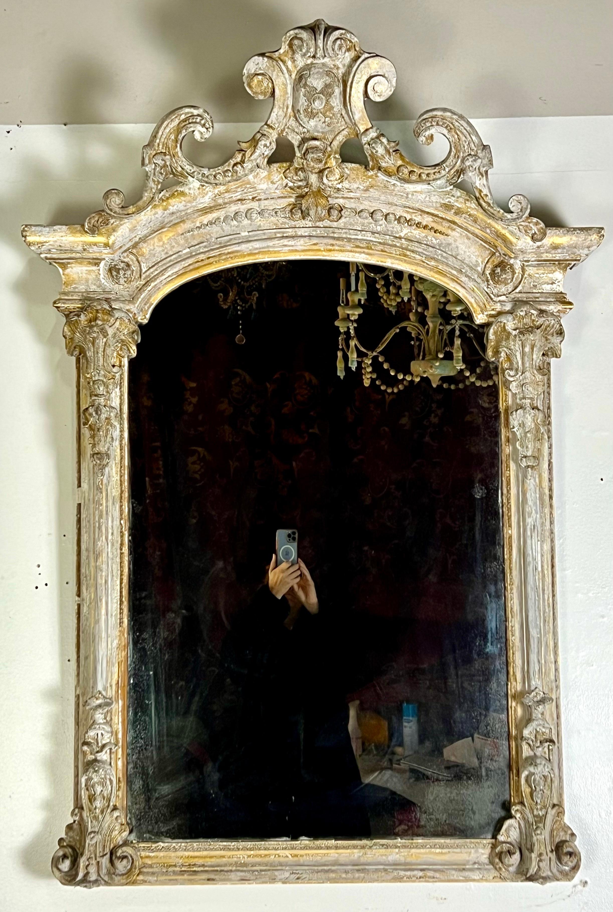 Miroir orné de style rococo français du 19e siècle, peint et doré parcellaire, caractérisé par ses rinceaux élaborés et ses motifs floraux. La finition peinte est vieillie et il y a des restes de feuilles d'or dans tout le cadre.
