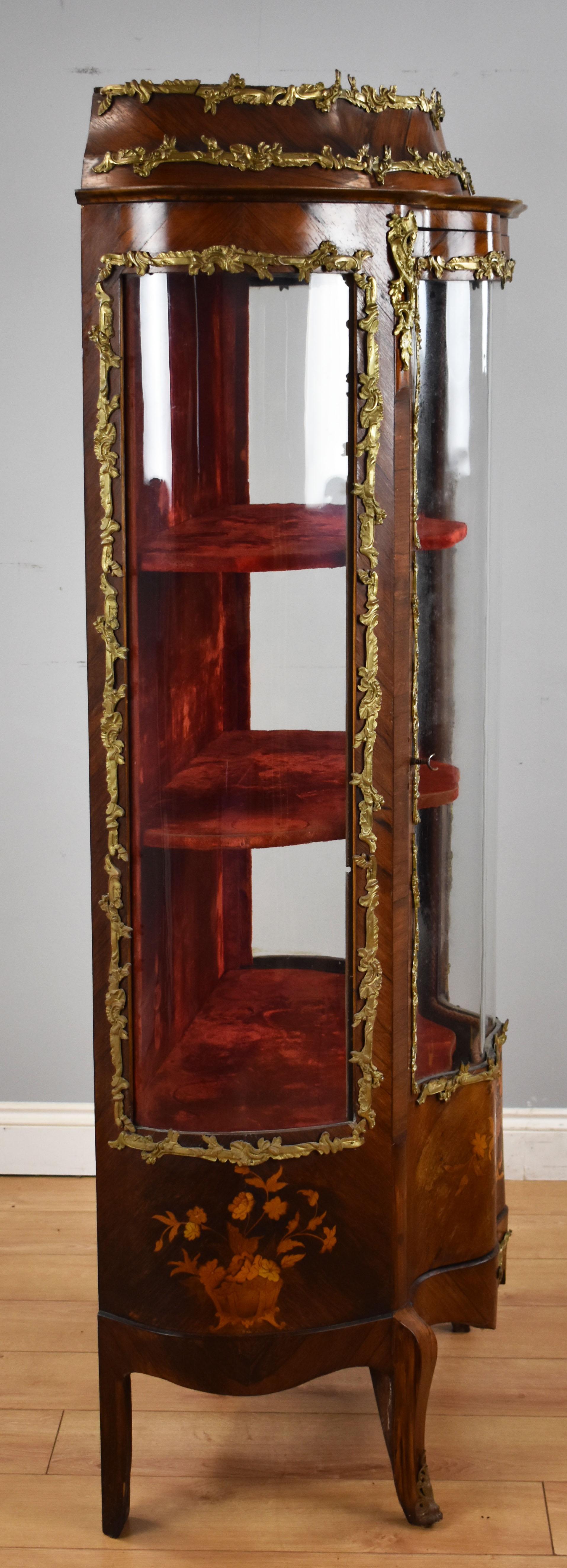 For sale is a good quality 19th century French marquetry serpentine fronted display cabinet. The cabinet is crowned with ormolu mounts, with more below. On each side of the cabinet is a bowed pane of glass displaying the rich velvet interior. The