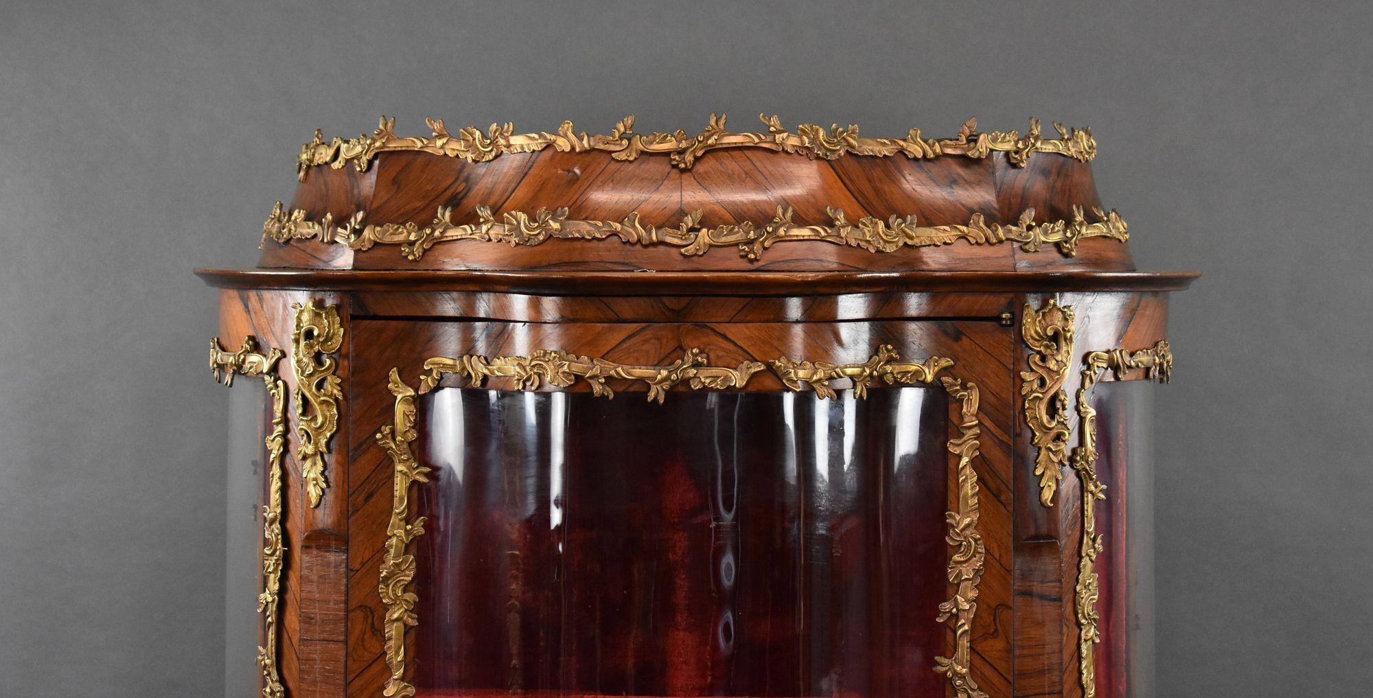 For sale is a good quality 19th century French marquetry serpentine fronted display cabinet. The cabinet is crowned with ormolu mounts, with more below. On each side of the cabinet is a bowed pane of glass displaying the rich velvet interior. The