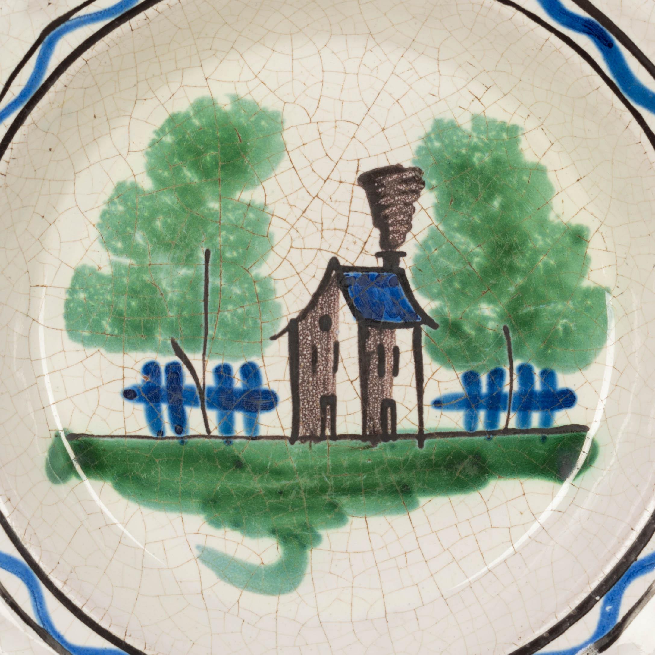 An early 19th century French glazed earthenware plate from Rouen, with a hand-painted country house in blue, grey and green. White craquelure ground and dark glazed back. Robust heavy pottery with a simple charming design. Please refer to photos for