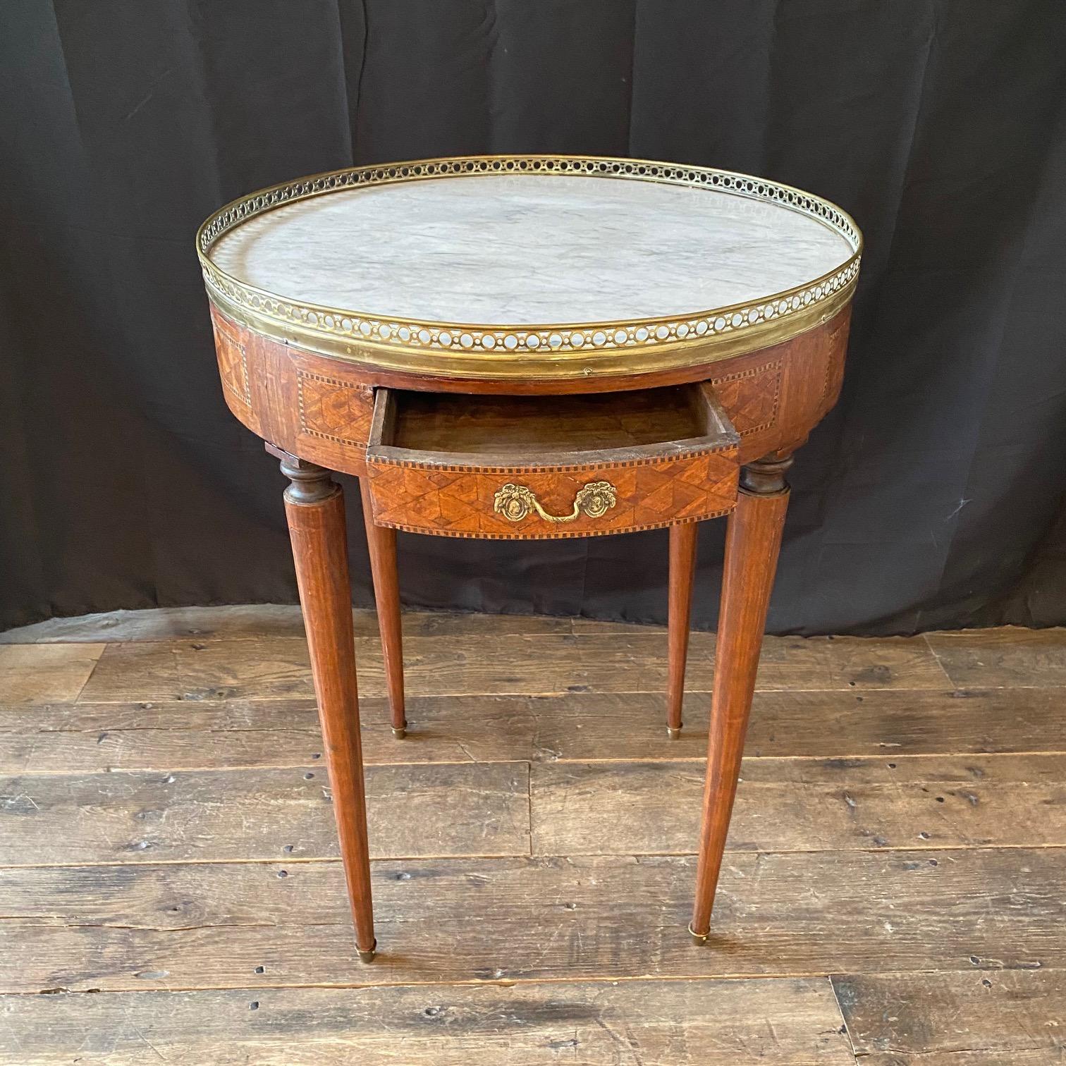 Louis XVI period round Carrara marble top accent table, round side table or bouillotte table with elaborate marquetry. Two drawers and two pull out tirelles or slides. White Carrara marble top is surrounded by a pierced bronze gallery. Absolutely