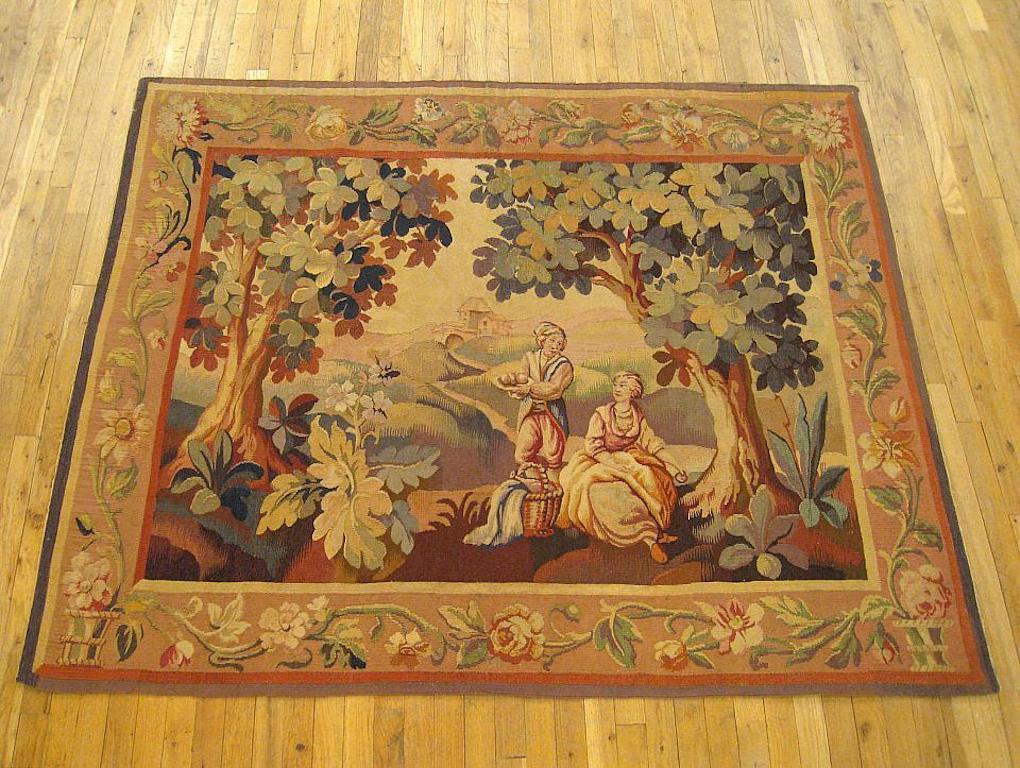 A French rustic landscape tapestry from the 19th century, portraying a young gentleman and his fair dame seated beside an acanthus plant under the shade of two large oak trees, perhaps picnicking or gathering fruit together in the sun-drenched hills