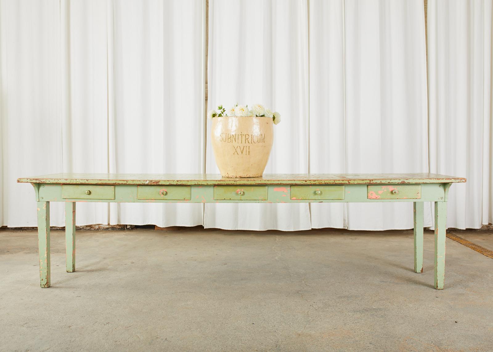 Large rustic late 19th century country French farmhouse work table or dining harvest table featuring a sage green painted finish. Crafted from long, framed planks the top measures over 9.5 feet long. The frieze has five storage drawers on one side