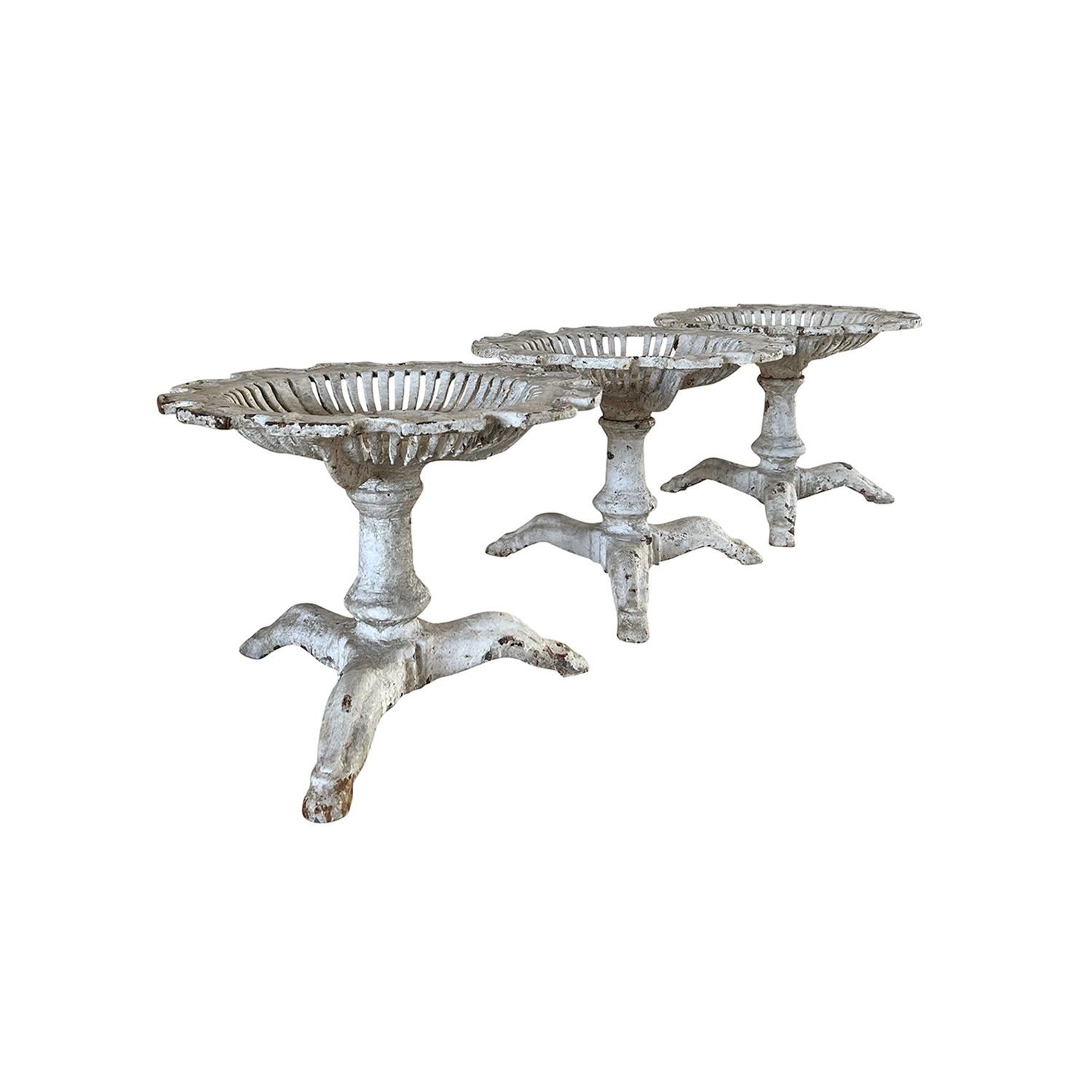 An antique French set of three elevated cast iron plant stands with detailed circular plates, scalloped rim detail, in good condition. The plates are elevated onto a tripod base. Original white grey patina. Minor fading, scratches due to age. Wear