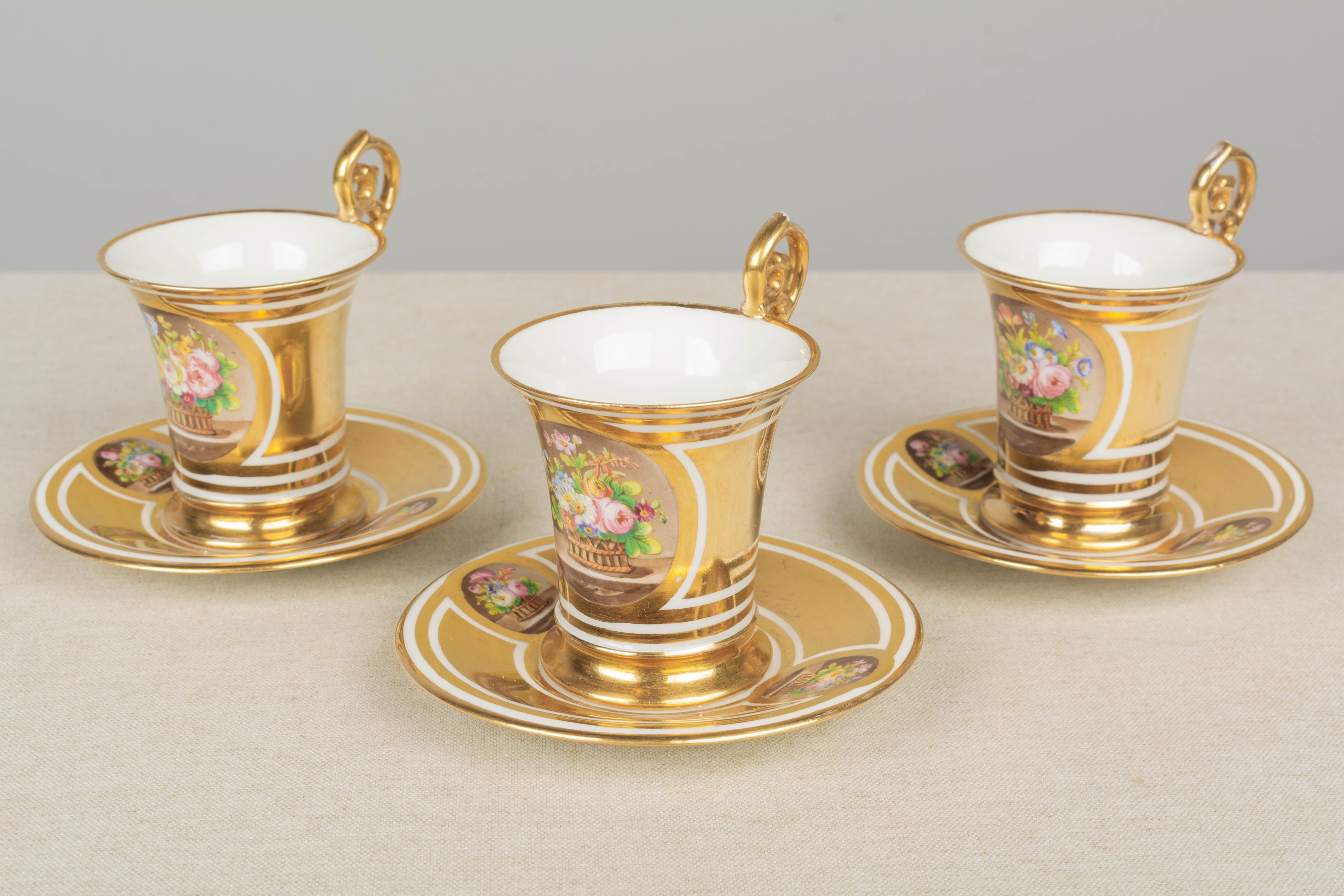 A set of three 19th Century French Sèvres fine gilded porcelain cups and saucers with tall scrolled handles. Hand-painted floral decoration. Sèvres mark to underside with red Château des Tuileries stamp. In good condition with light rubbing to gilt.