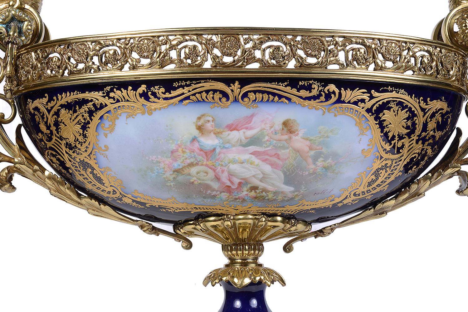 A good quality late 19th Century French Sevres style porcelain comport, having gilded ormolu classical female mounted handles on either side, above a pierced collar, a cobalt blue ground with gilded decoration, inset painted panels depicting a