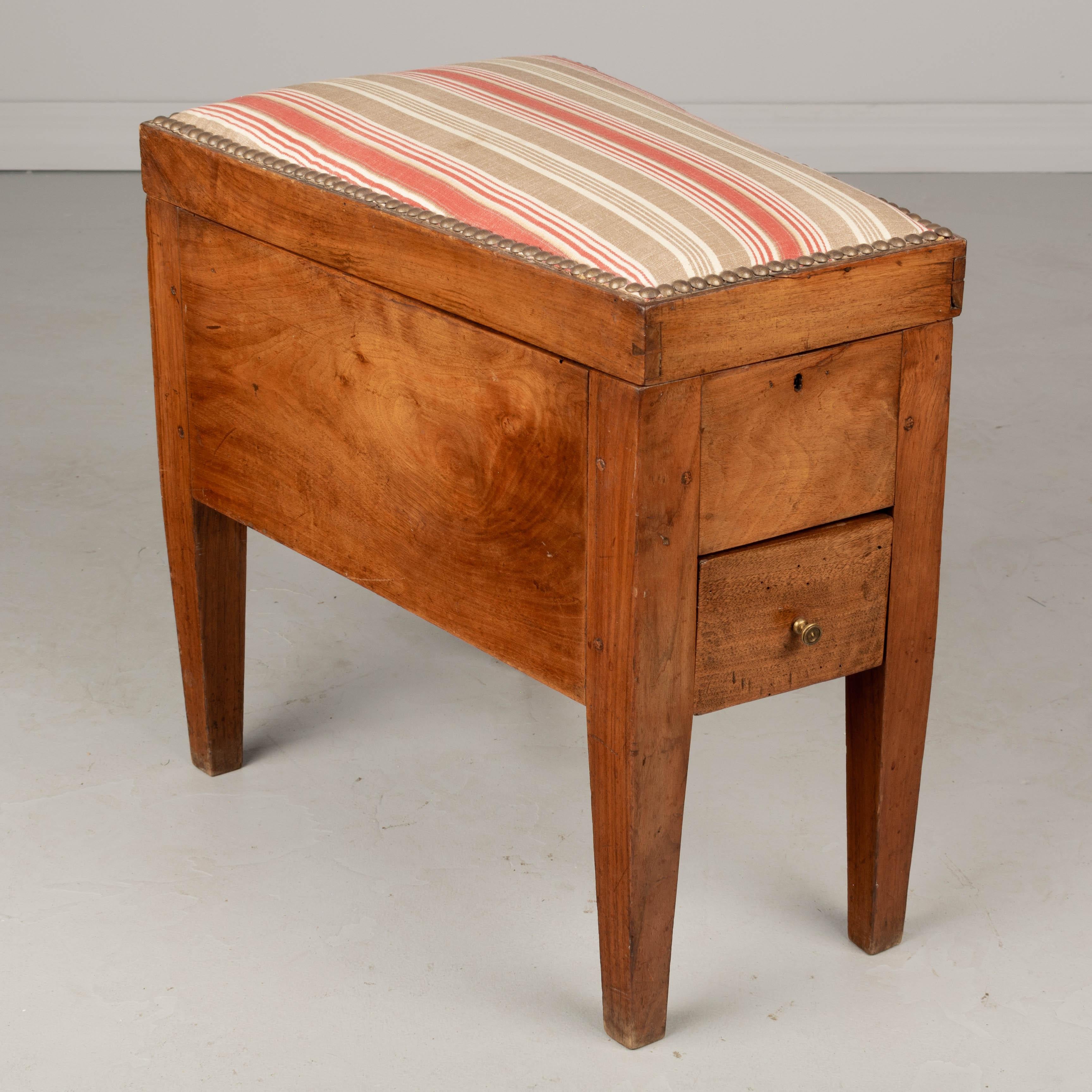 A 19th century French shoe shine stool made of solid walnut. The upholstered seat opens to a felt lined interior for storing polish and brushes. Small drawer below with brass pull. Pegged construction and sturdy dovetailed frame. New brass hinges.