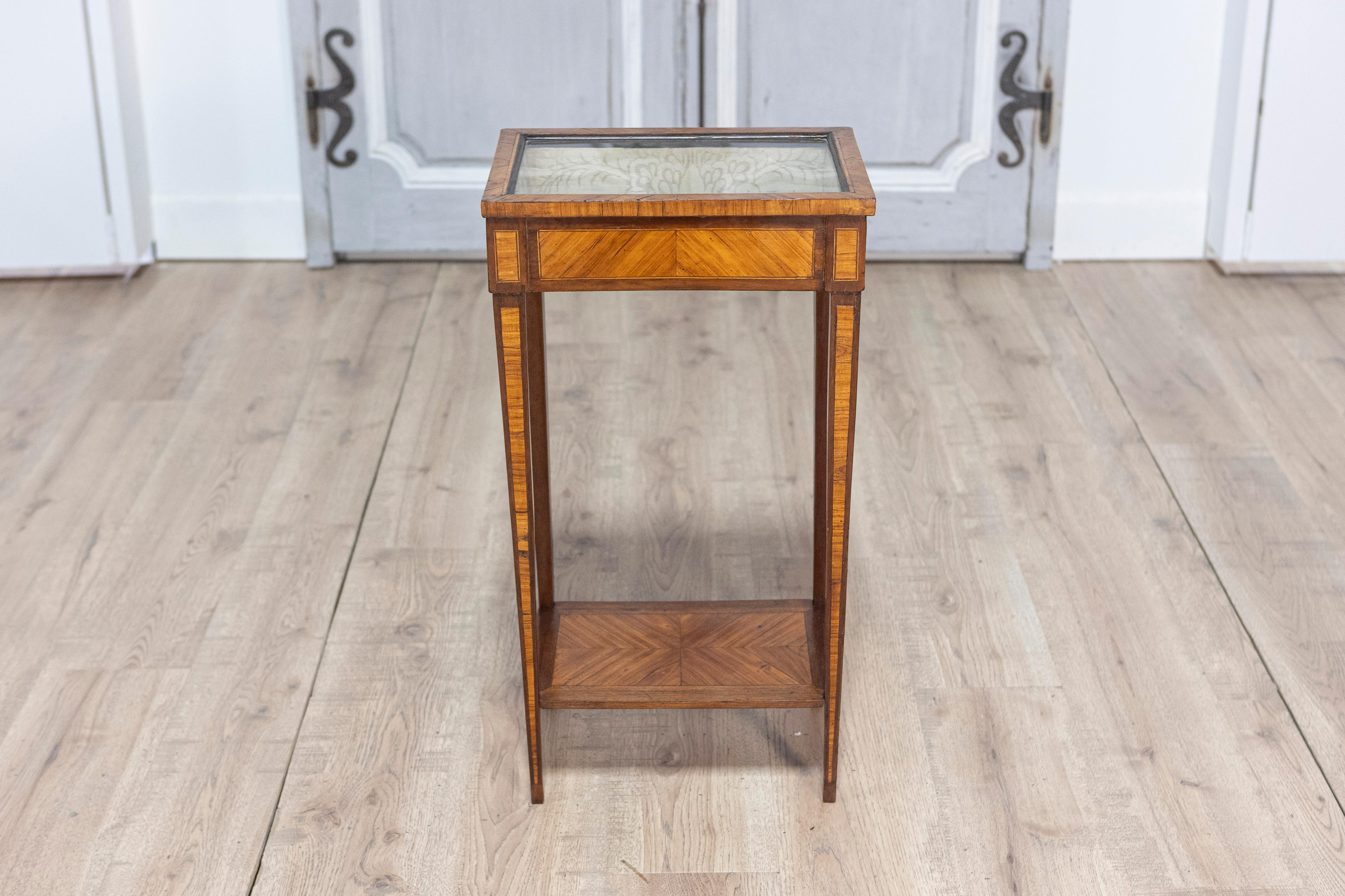 Dieser Vitrinentisch im Louis-XVI-Stil aus dem 19. Jahrhundert ist ein raffiniertes Beispiel für Handwerkskunst und Eleganz. Das mit Intarsien verzierte Äußere wird von einer originalen Glasplatte gekrönt, die sich öffnen lässt, um ein mit der