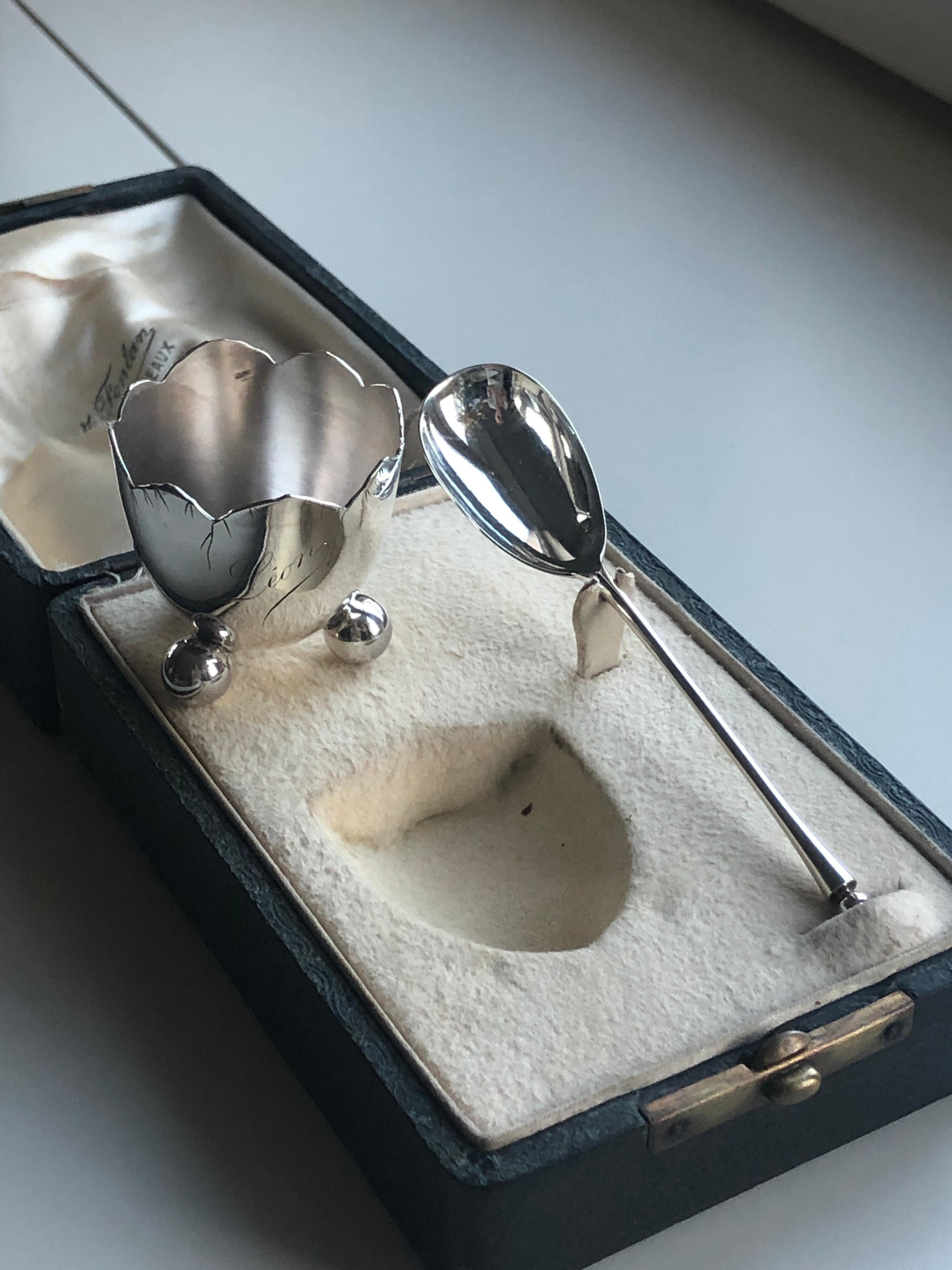 Silver egg cup and silver spoon, it rests on three feet balls and the belly is marked 