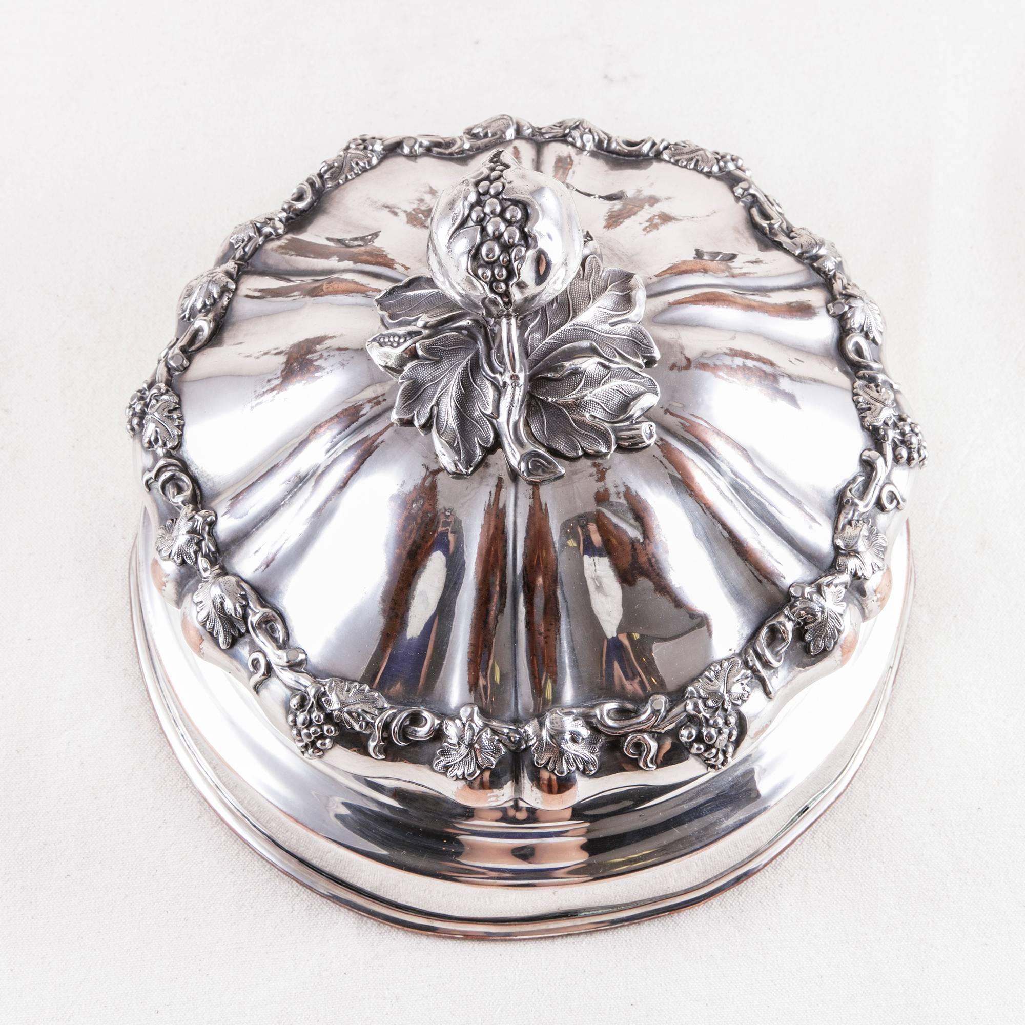 This elegant French hotel dome is lavishly adorned with a band of scrolling grape vines and hanging bunches of grapes. Its top handle is a pomegranate resting on a bed of leaves. Silver plated over copper, this elegant serving piece was originally