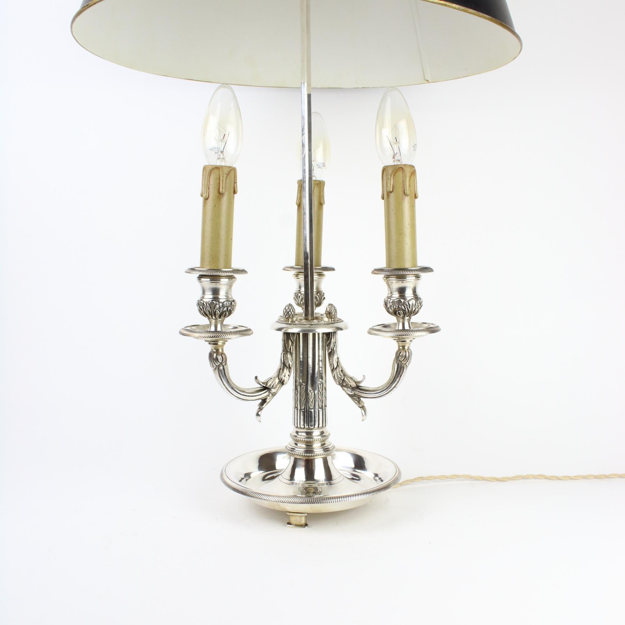 19th Century French silver plate Louis XVI three-light bouillotte table lamp.

A 19th century Louis XVI style silver plate bouillotte lamp fitted with a black toleware lampshade, with a circular fluted stem supporting three scrolled foliate candle