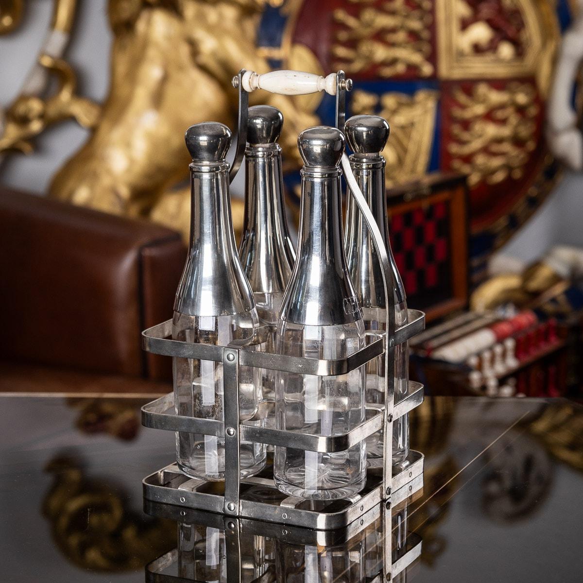 Antique late-19th century French four bottle Tantalus, clear glass applied with silver plated mounts and stoppers. The tops are engraved with various drinks, such as curacao, anisette, chartreuse and fine champagne. The four bottles are presented in