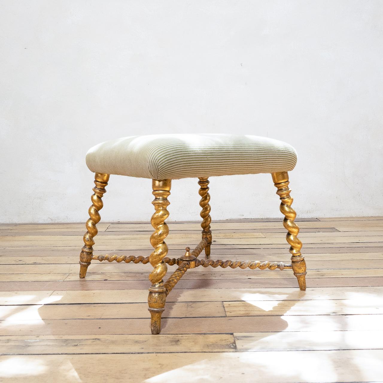 A 19th century French giltwood and upholstered stool, circa 1850. Displaying a square seat above four out-splayed barley twist legs united by conforming stretchers with a central turned finial. 

Measures: Height 47cm 
Seat 50cm- Square.