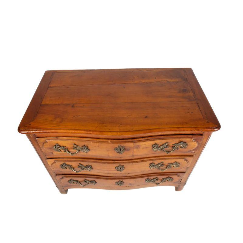 A 19th Century French style three drawer dresser with detailed brass hardware.  Each drawer face is decorated with a notched oval raised panel and ornate scroll motif drawer pulls and key holes. Top of chest is constructed of three panels bordered