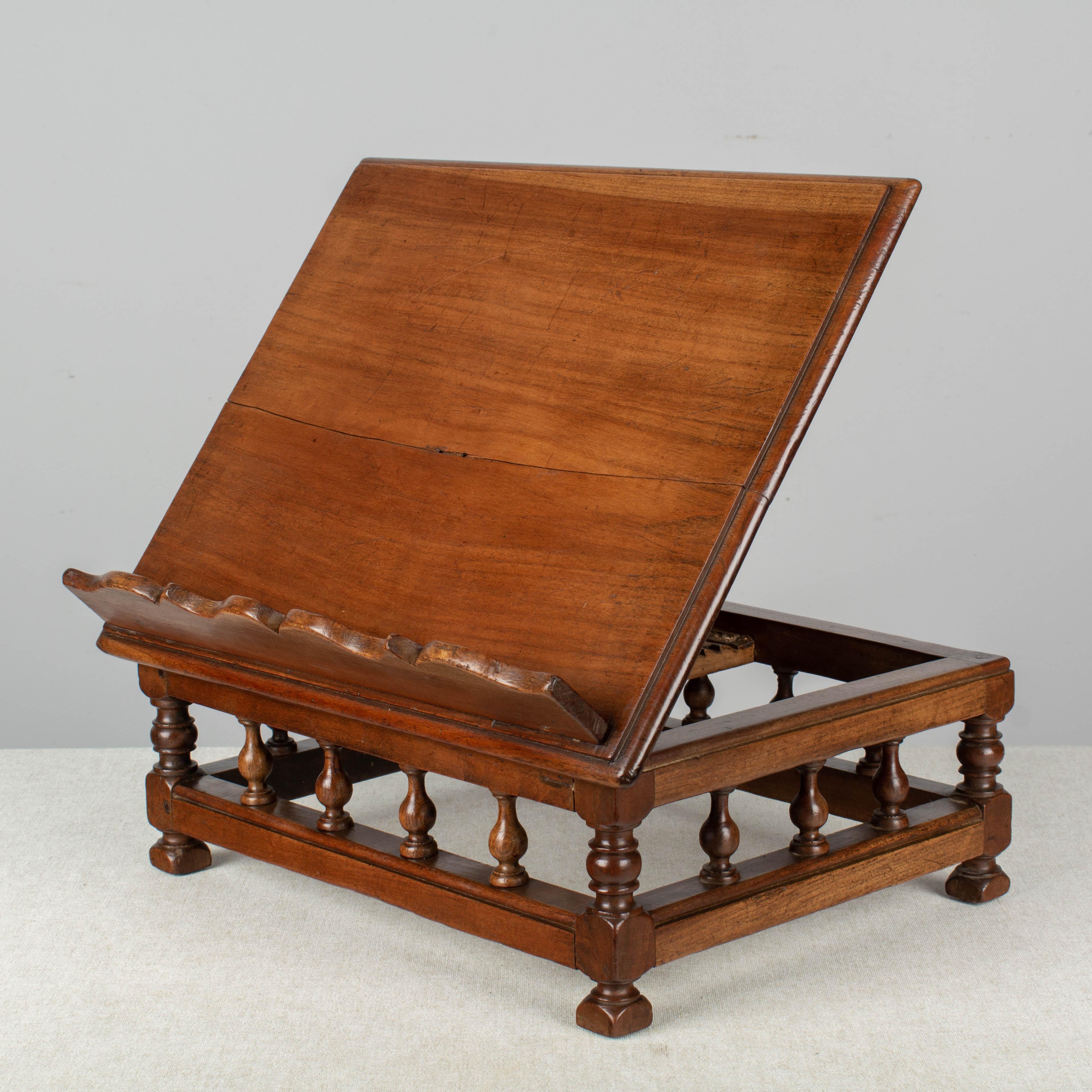 A 19th century French tabletop book stand with adjustable easel and scalloped ledge made of cherry and walnut. An iron hinge on the back and multiple notches allows the plank to be propped to a variety of angles. Sturdy base decorated with turned