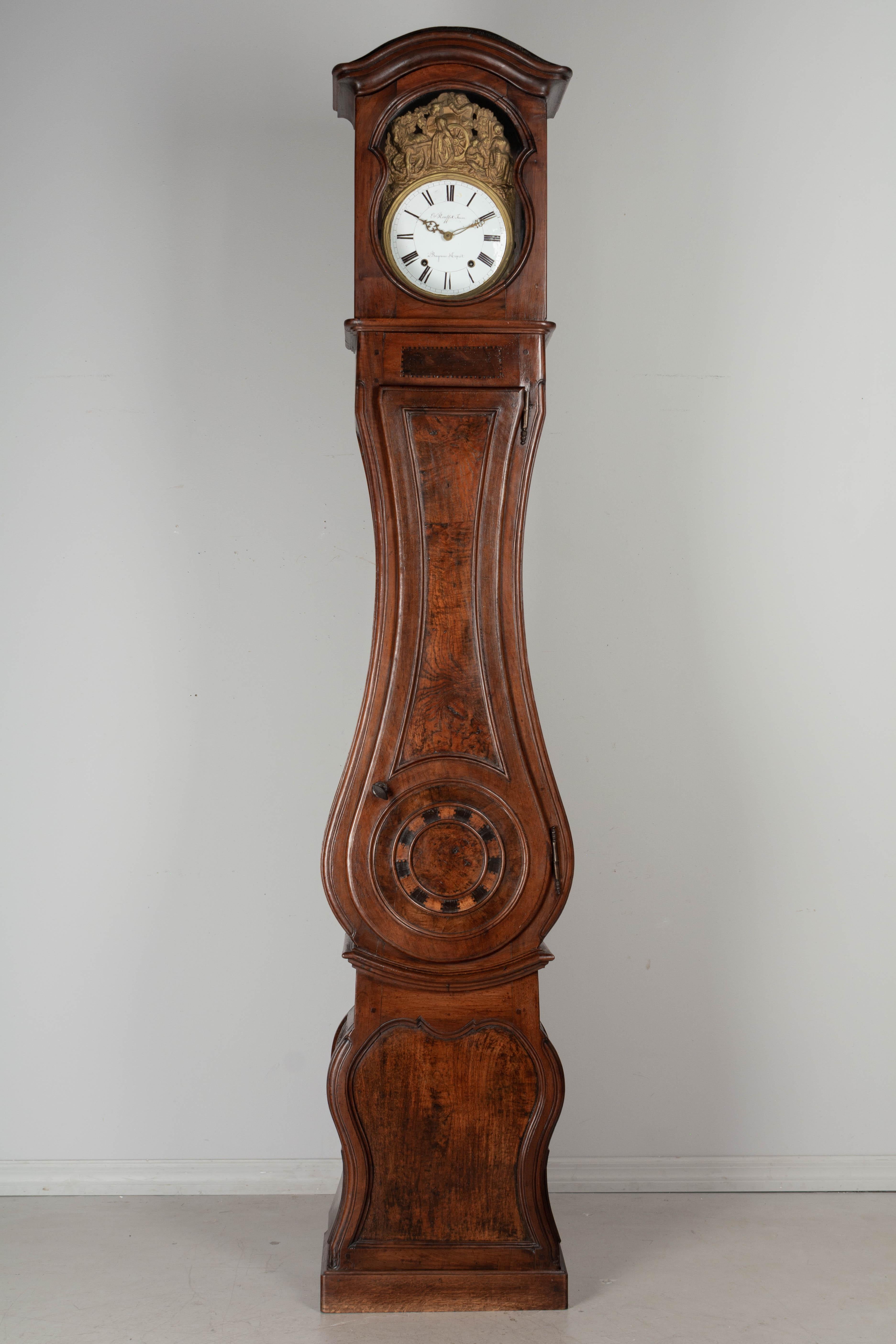 A 19th century French Horloge De Parquet, or tall case clock, from Burgundy. The case is made of solid walnut with marquetry inlay details. In two parts with a curved shaped body, paneled sides and a chapeau de gendarme crown. Original glass panes.