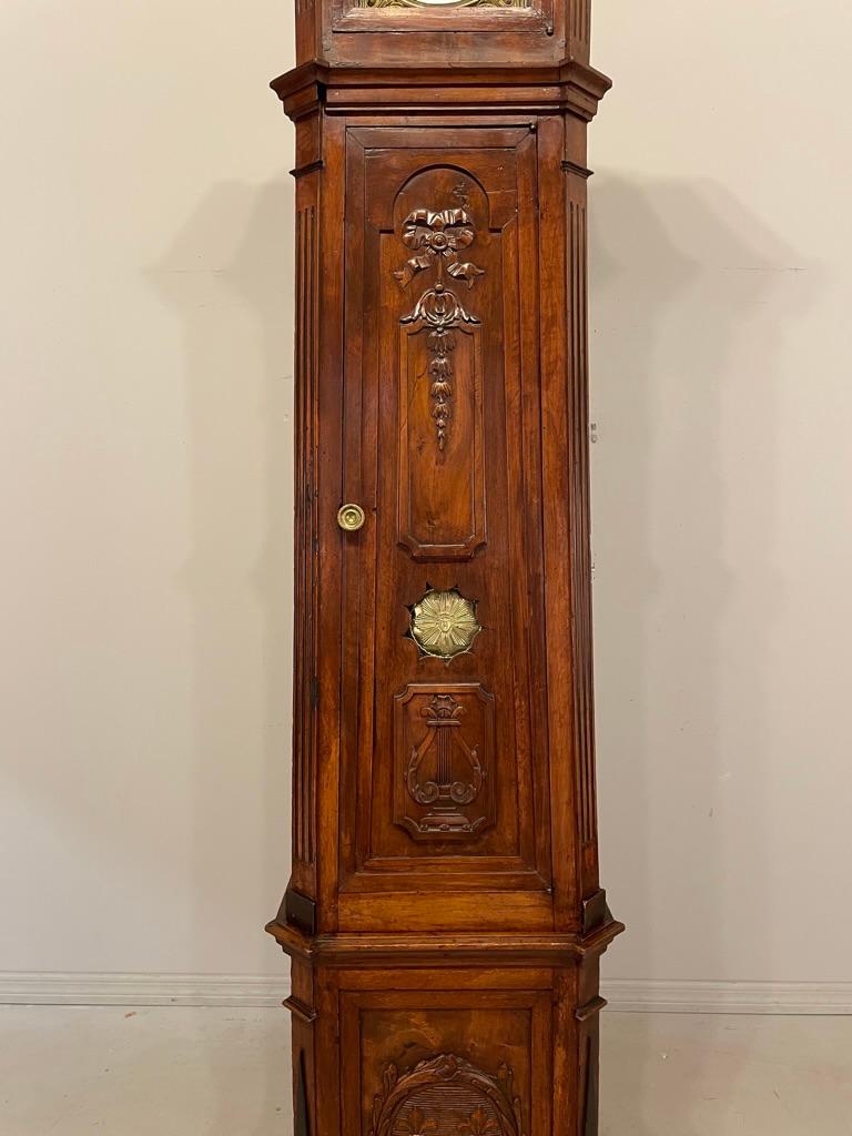 A fine early 19th century French Horloge De Parquet, or tall case clock, from Provence made of solid walnut. The case is in three parts with paneled sides and beautiful hand carvings: a trio of fleur-de-lis at the base and a lyre and ribboned floral