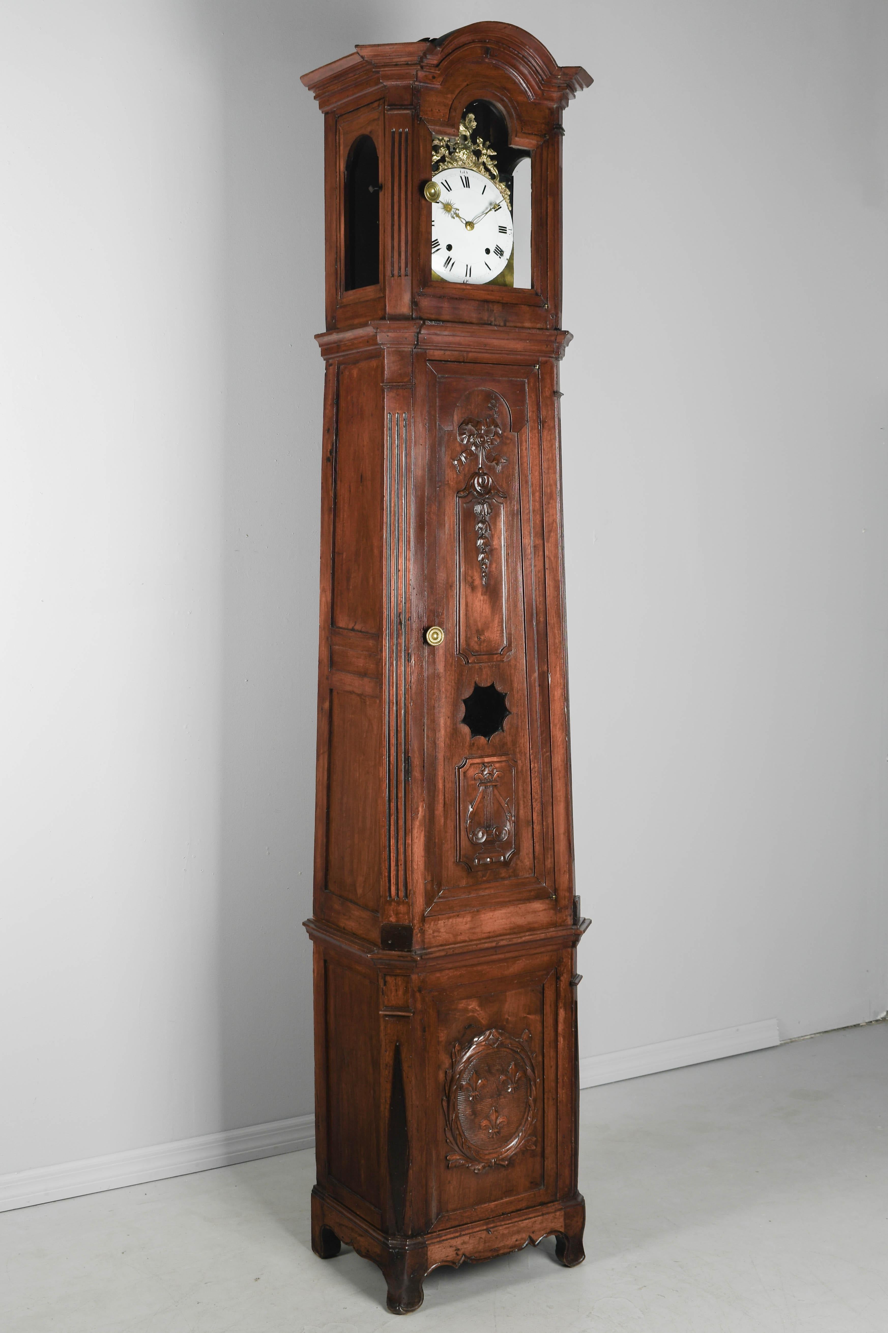 A fine early 19th century French Horloge De Parquet, or tall case clock, from Provence made of solid walnut. The case is in three parts with paneled sides and beautiful hand carvings: a trio of fleur-de-lis at the base and a lyre and ribboned floral