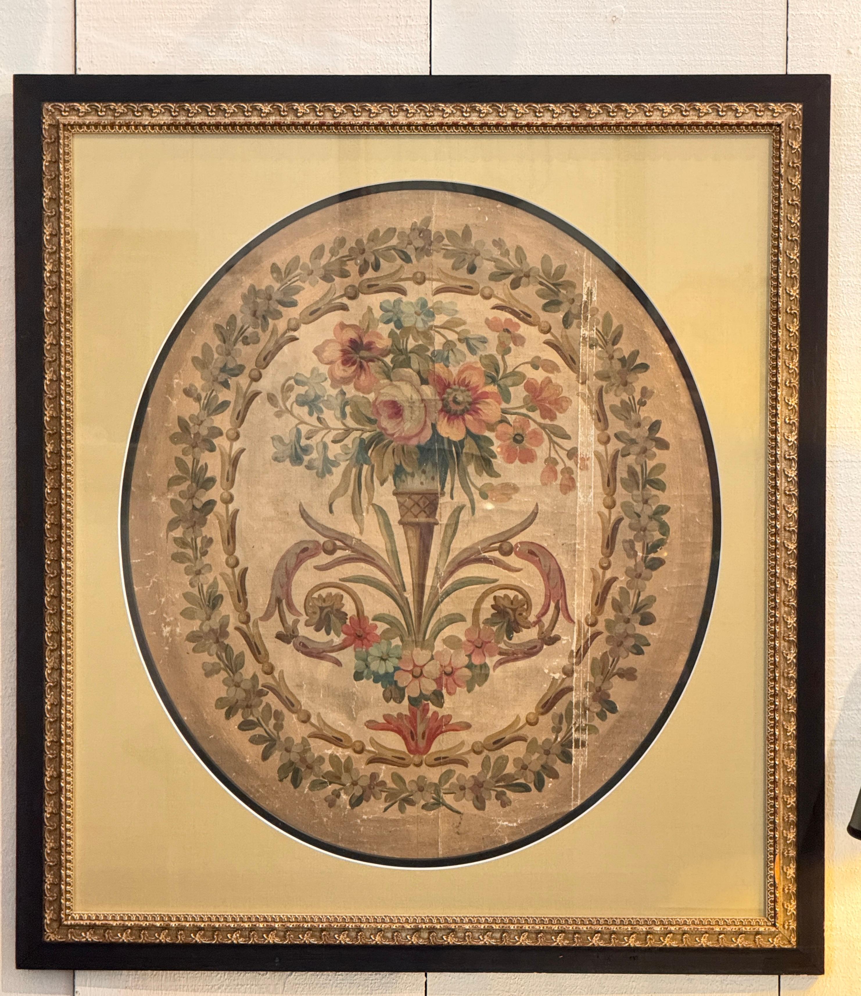 Un cartone da arazzo francese del XIX secolo con un'urna centrale traboccante di fiori, circondata da un bordo foliato e da dettagli a volute. Esposto in un formato rotondo e montato in una cornice dorata e nera con tappeti di seta. L'età e l'usura
