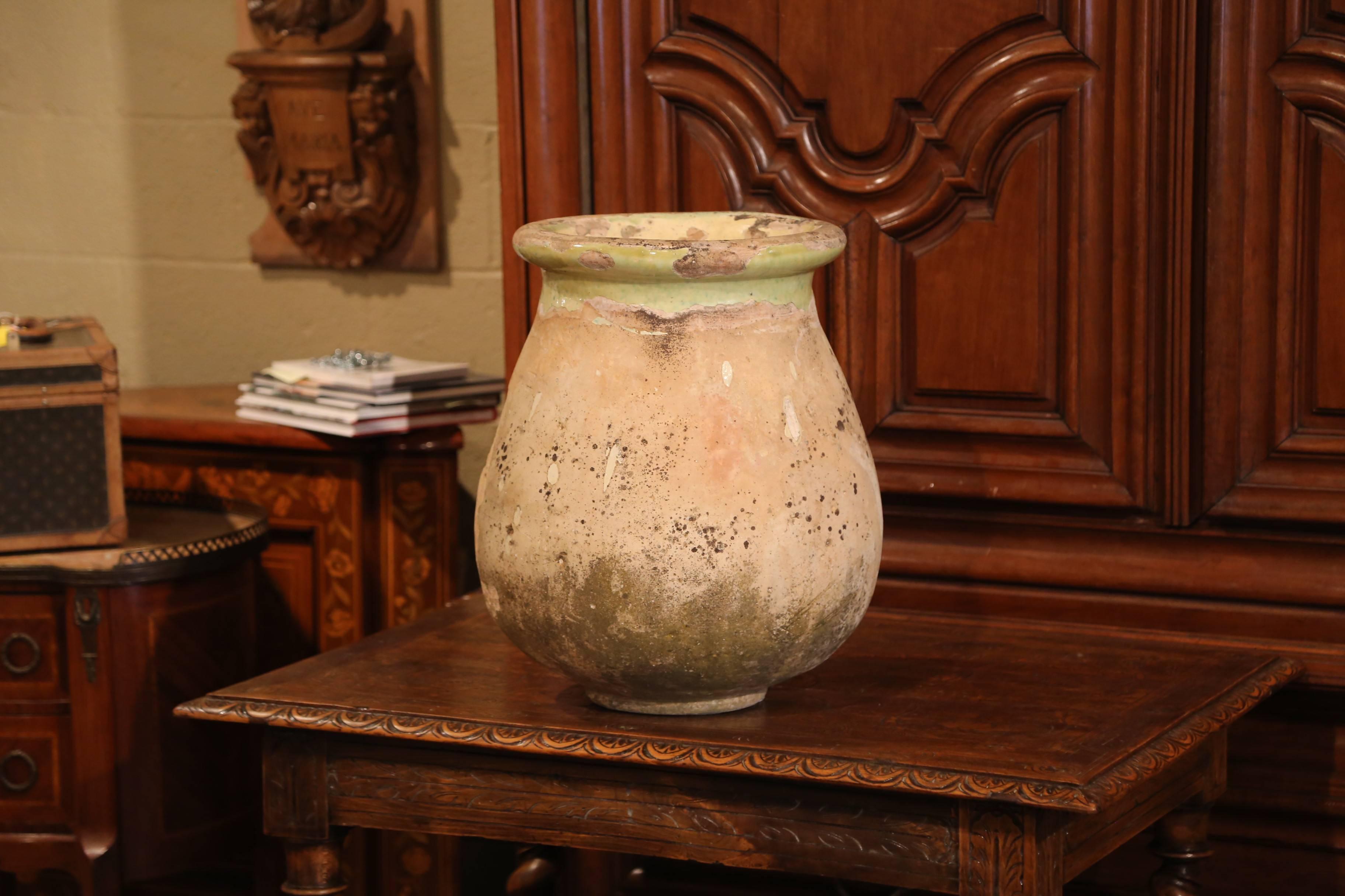 This antique earthenware olive jar was created in Southern France, circa 1860. Made of blond clay and neutral in color, the terracotta has a traditional round shape; the pot features a yellow glaze around the neck and trim, and a natural beige tone