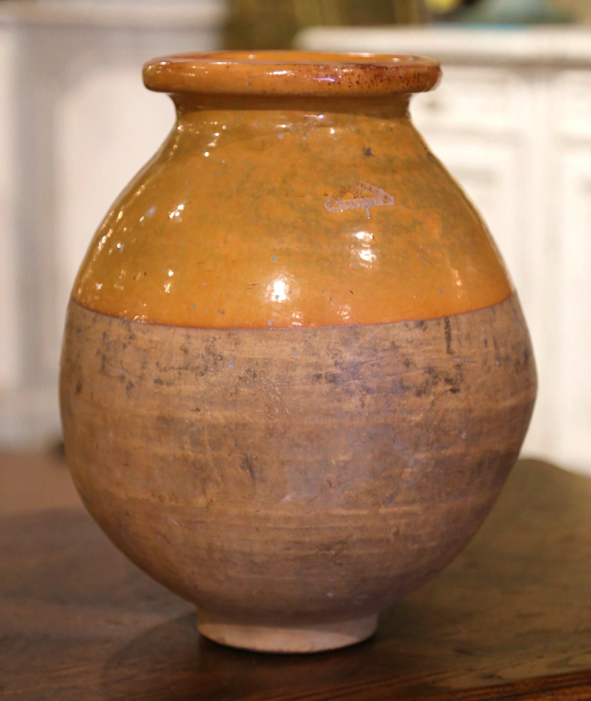 This antique earthenware olive oil jar was created in Southern France, circa 1880. Made of blond clay and neutral in color, the terracotta vase has a traditional round shape. The rustic, time-worn pot features a yellow glaze around the neck and