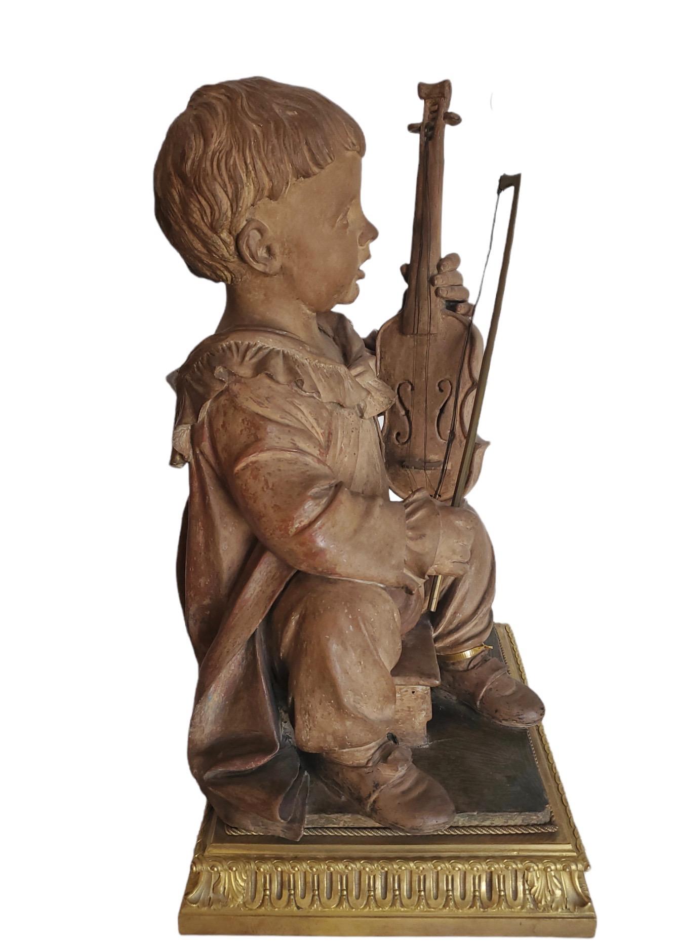 Figurine en terre cuite finement sculptée représentant un garçon jouant du violon. Elle repose sur un socle séparé en bronze doré français finement moulé.