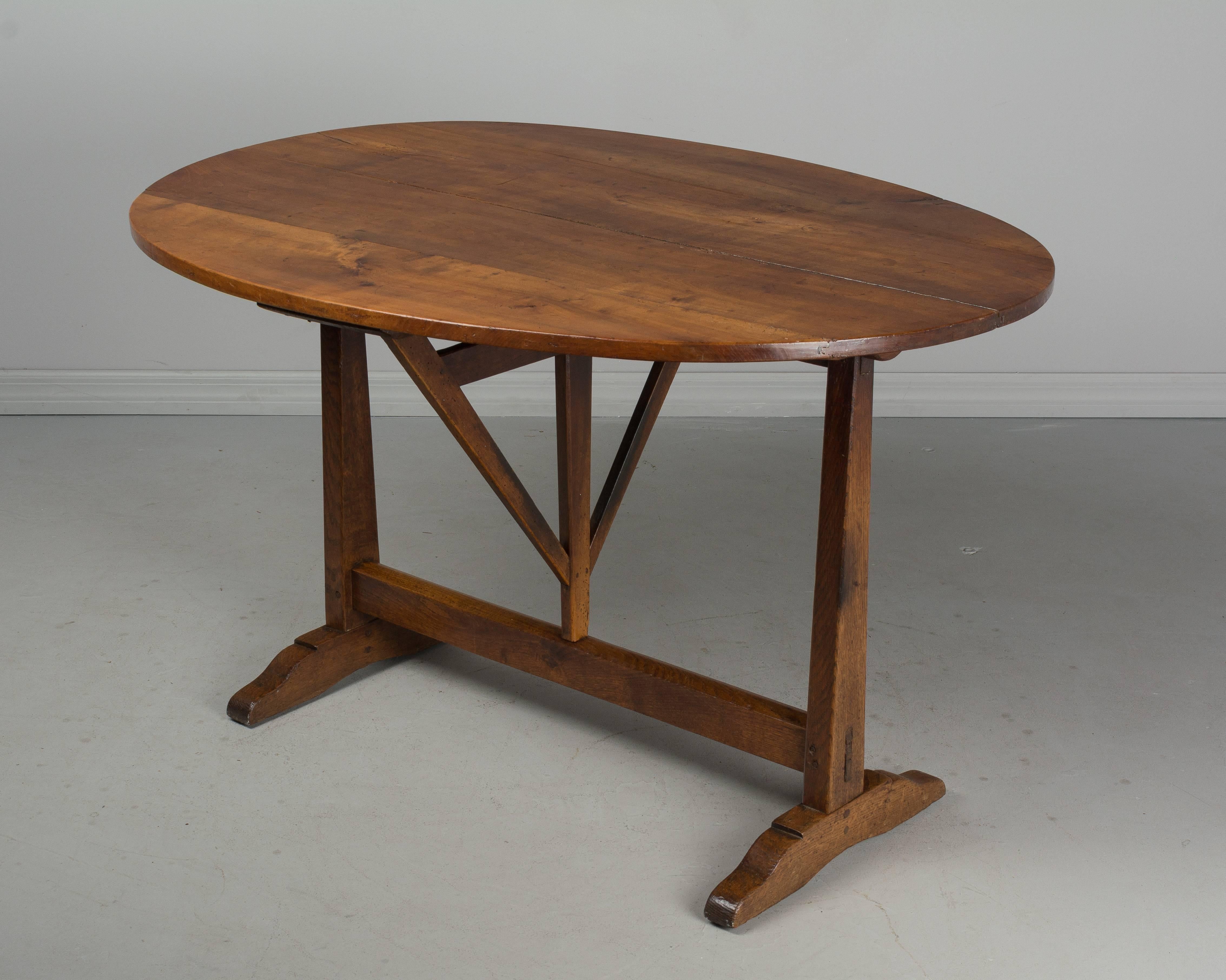 A 19th century French tilt-top oval wine tasting table with a top made of four planks of cherrywood and an oak base. Sturdy and well crafted with beautiful wood grain. In good condition with a slightly warped surface and with normal shrinkage on the