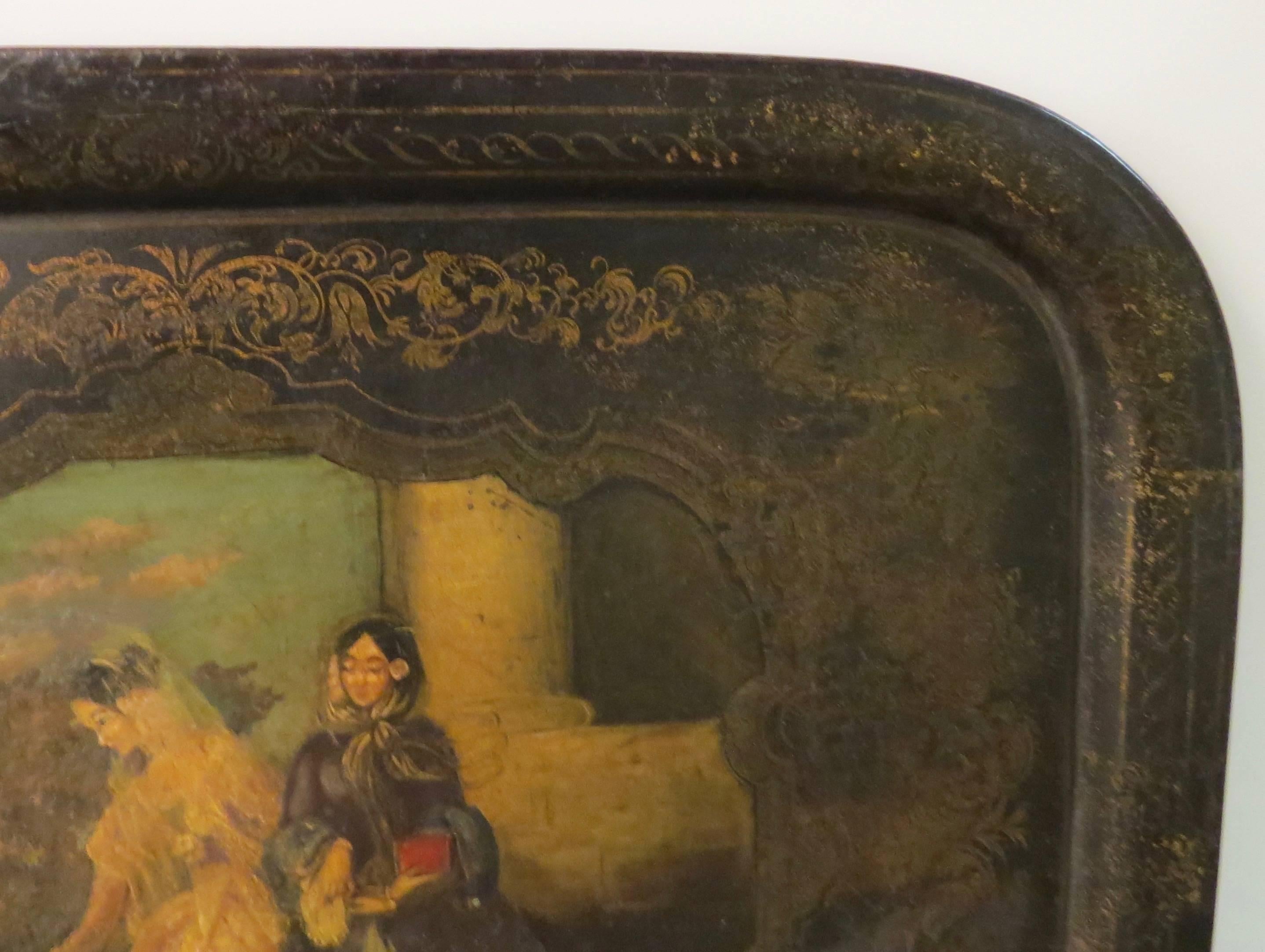 Rectangular tole tray with black background. Delicate floral border in gold. Central scene depicting two elegant ladies offering a donation to a kneeling man, 19th century origin. Painting is in good condition, perhaps it has been well cleaned or