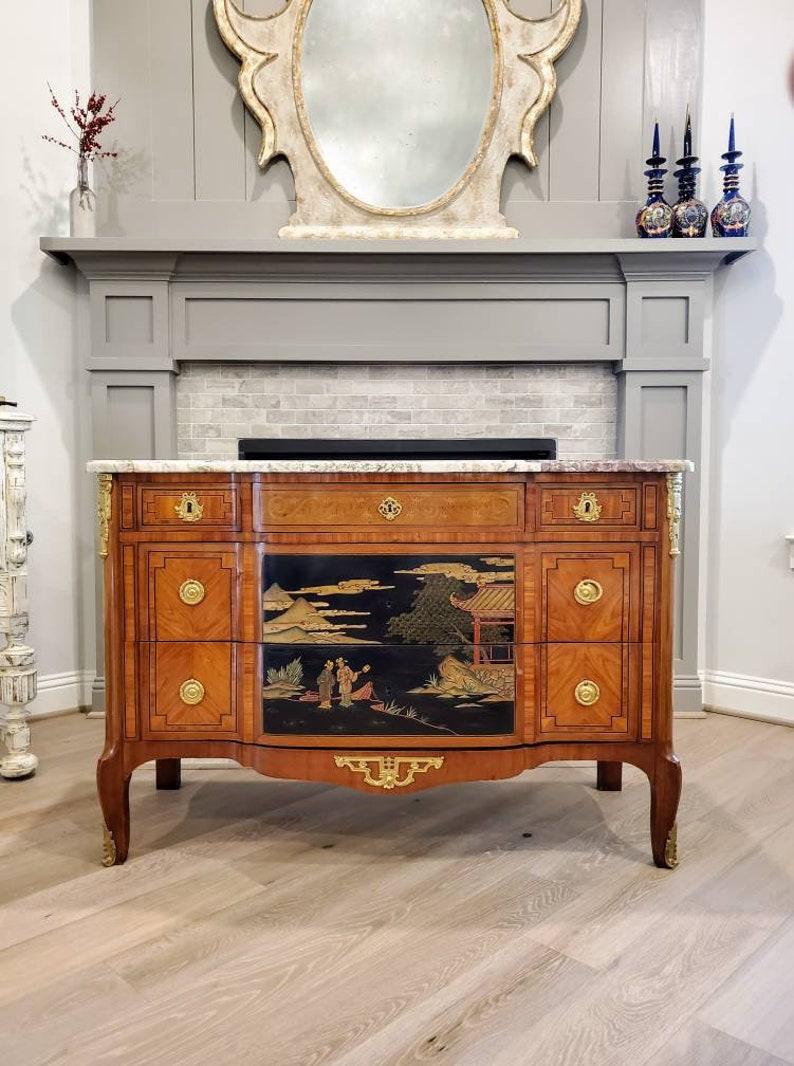 We present a rare and elegantly sophisticated Louis XV - Louis XVI Transition style chinoiserie black and gold lacquered and gilt bronze mounted breakfront chest of drawers. Born in France in the 19th century, the fine quality mahogany inlaid