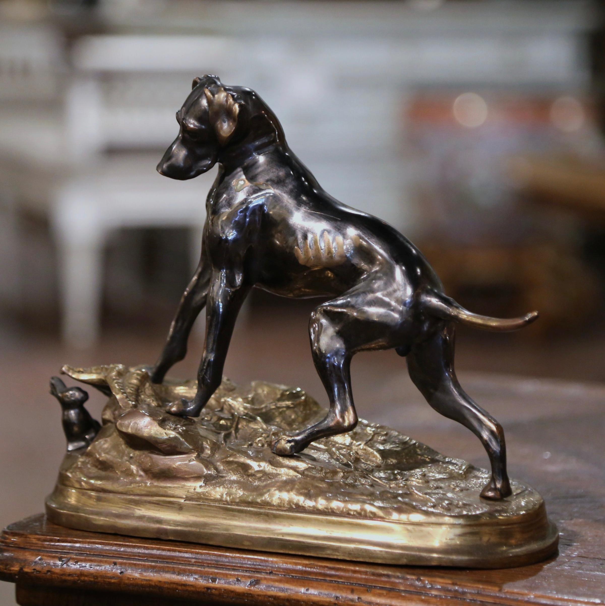Cette sculpture ancienne en bronze a été créée en France, vers 1880. Posée sur une base en bronze doré, la composition présente un chien labrador en bronze patiné, debout sur un sol rocailleux, jouant avec un petit lapin caché derrière un feuillage.