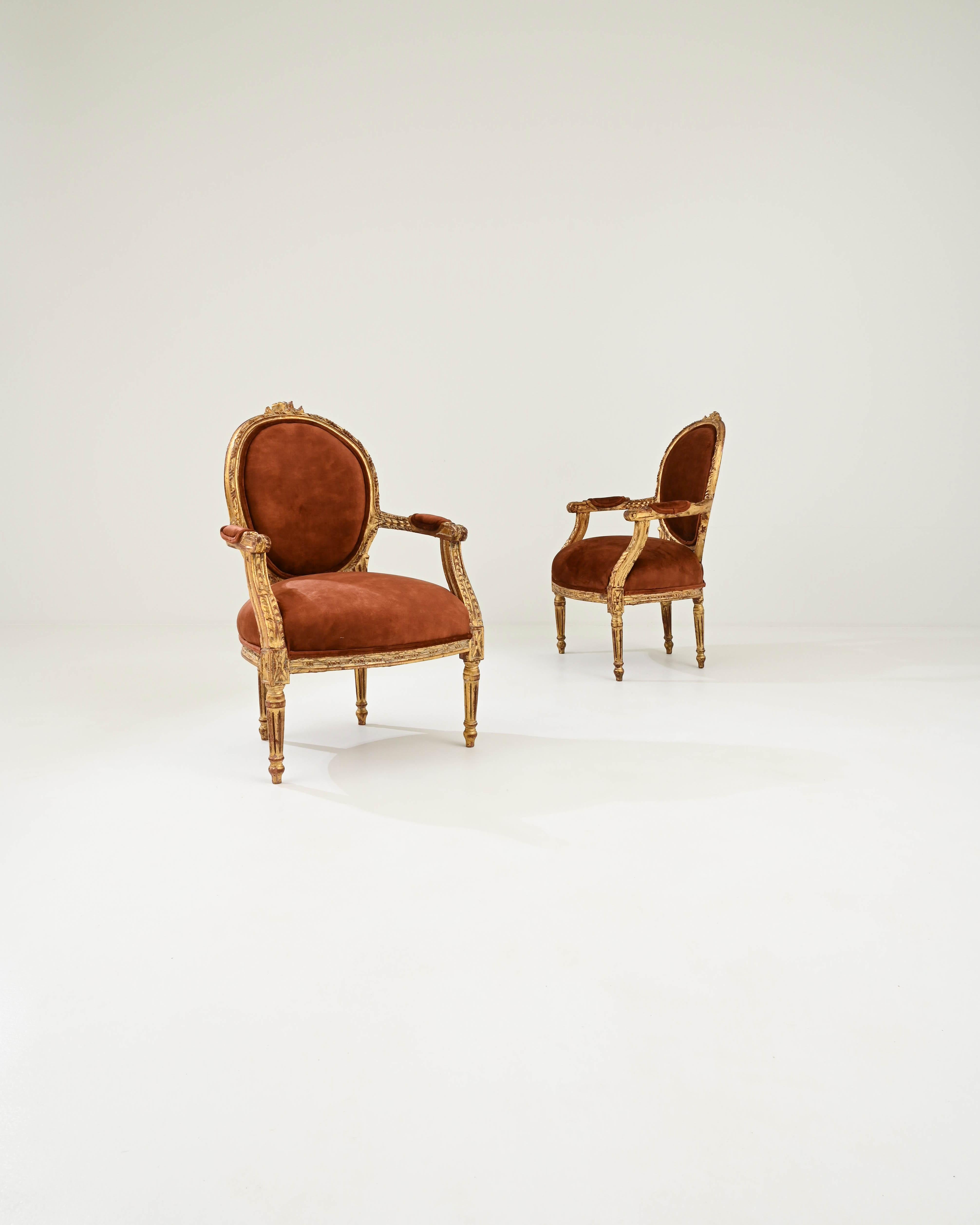 Radiating a pronounced Rococo influence, this exquisite pair of armchairs was handcrafted in 19th-century France. The puffy seats upholstered in high-quality cognac-toned velvet, rest upon ornate wooden bases gilded with gold leaf. From the graceful