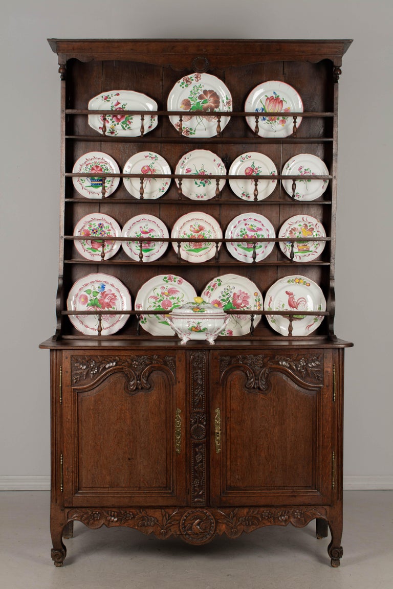 A 19th century Louis XV style Country French vaisselier, or hutch, from Normandy made of solid oak with beautiful hand carvings. The plate rack has three shelves with railings of turned wood spindles. The buffet has beautifully hand-carved floral