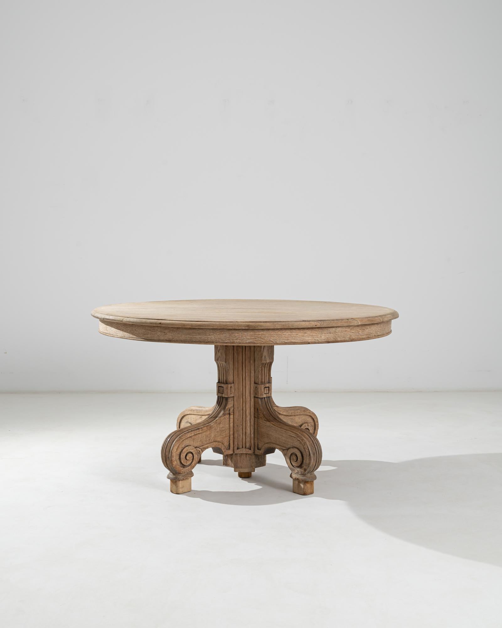 This French antique table boasts a flawlessly round table top raised on an ornate base with four volute-legs carved out of solid oak. A natural pale tone of the bleached wood dramatizes the flowing effect created by the meticulous carvings