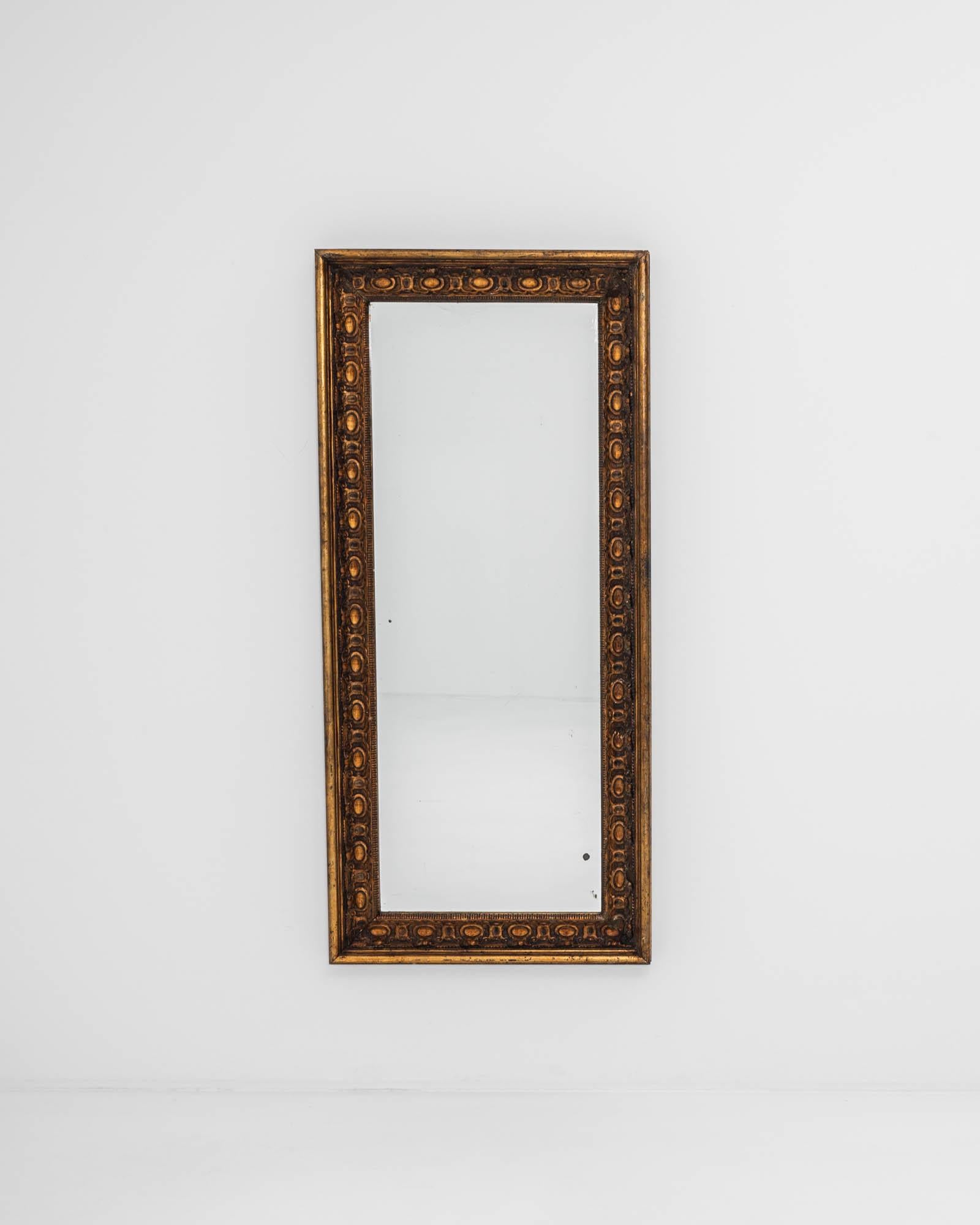 A wooden mirror created in 19th century France. Proudly aged, the paint has worn to a rich patina, blending darks tones and golden browns that shine in accord with a patinated gold leaf around the patterned frame. This one of a kind mirror combines