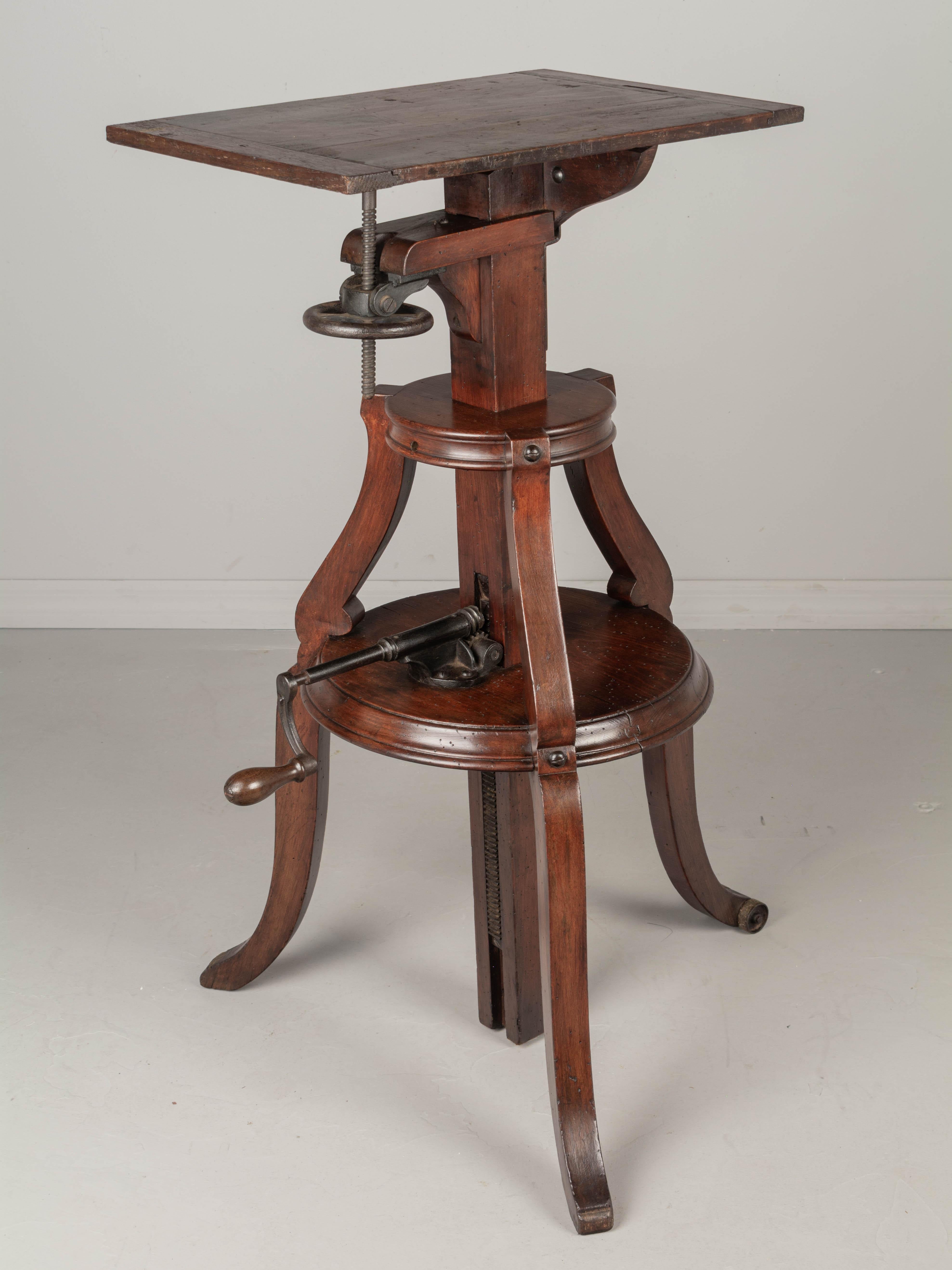 A 19th Century French adjustable sculptor's stand made of solid beechwood with dark finish and waxed patina. Rectangular top and sturdy tiered triform structure with splayed legs. One leg with roller wheel, so this heavy stand may be easily moved.