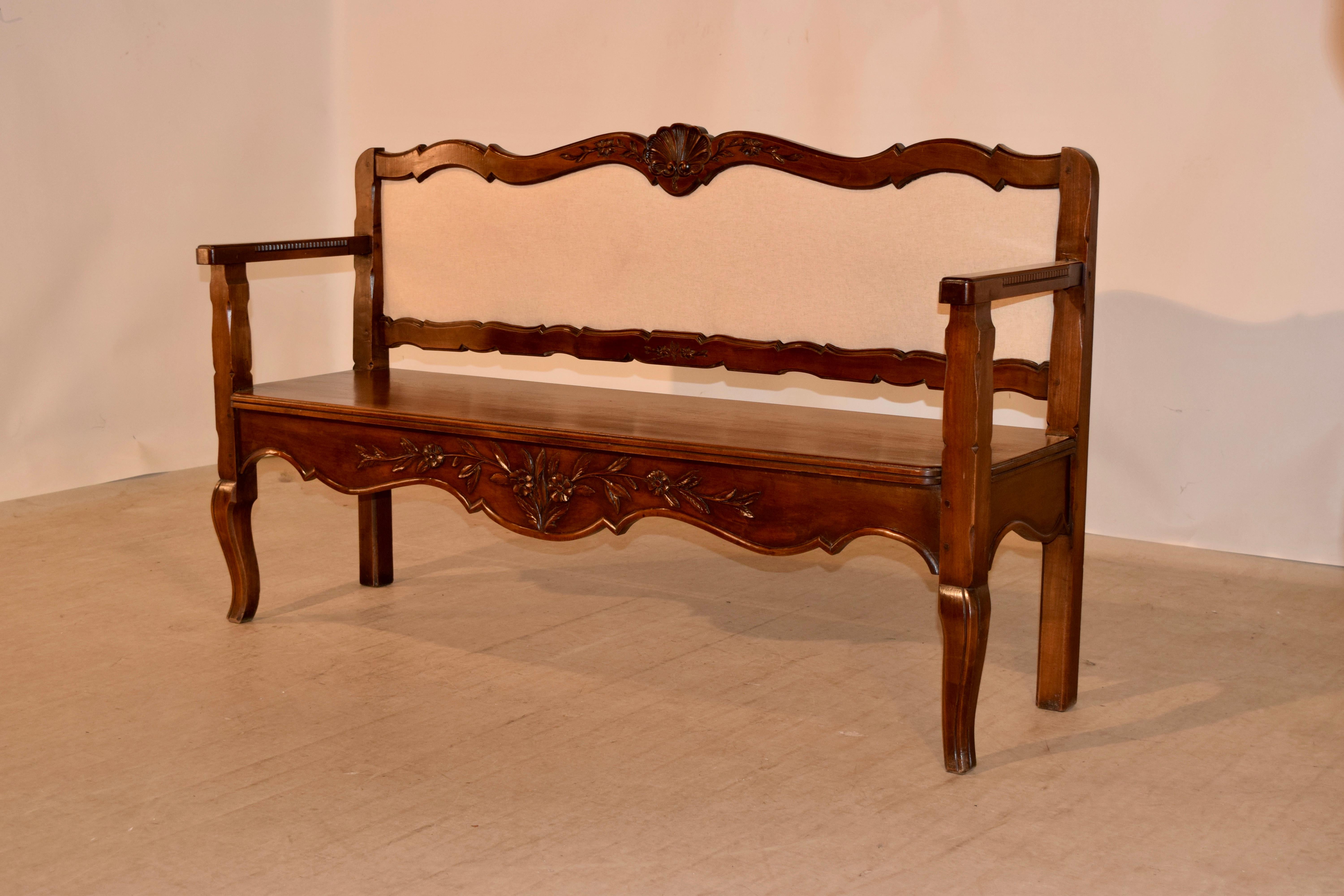 19th century walnut bench from France with a scalloped and hand carved frame with an upholstered back newly covered in linen following down to a solid walnut seat supported on cabriole carved legs in the front and solid legs in the back and a