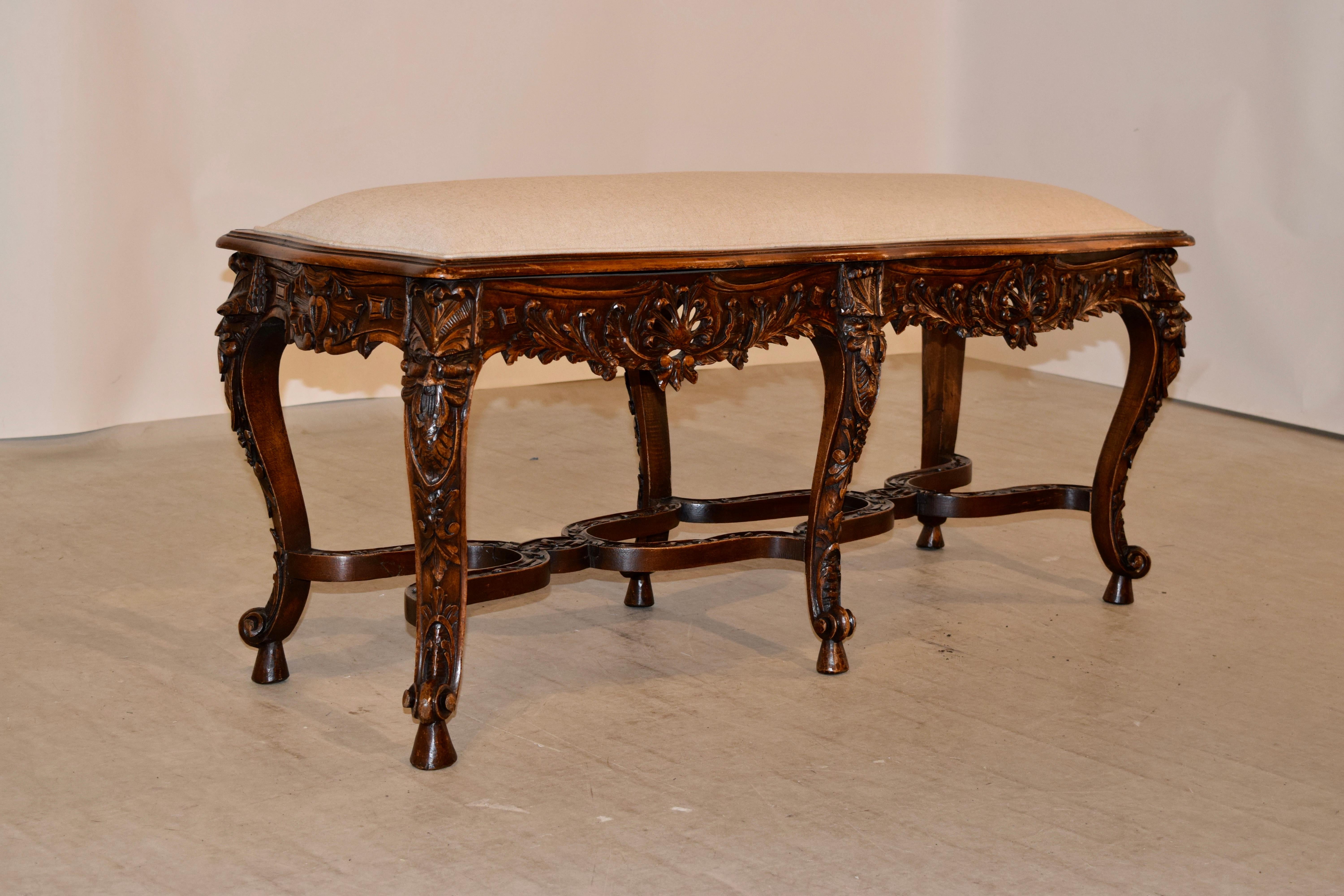 19th century carved walnut bench from France with a newly upholstered seat in linen and finished with welted decoration. The upholstered seat is scalloped and is enclosed in a molded and scalloped frame around the edge. This follows down to a