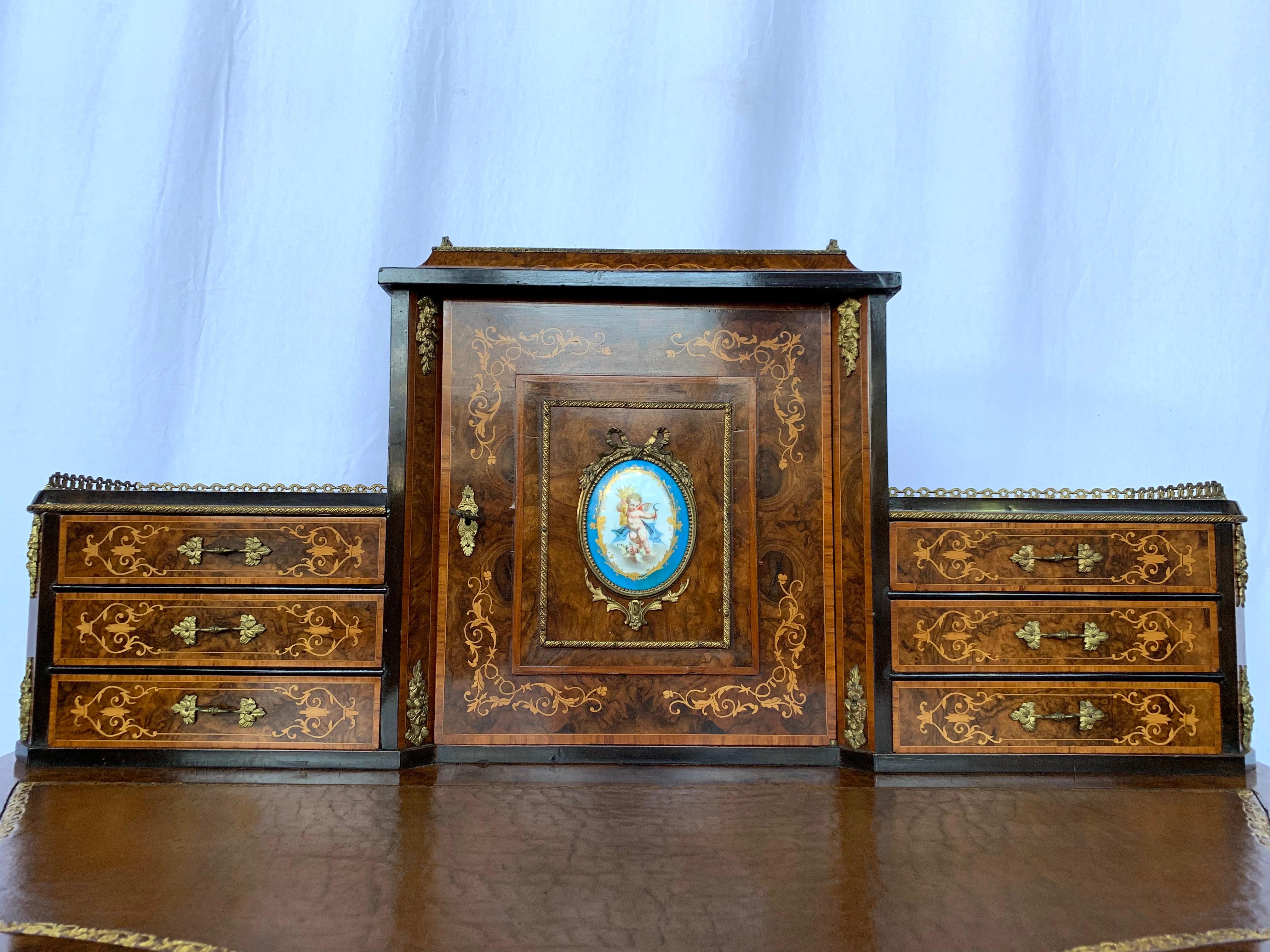 A French Walnut Bonheur du jour. Probably 19th century. The central cupboard inset with a porcelain plaque and flanked by two sets of drawers with a leather writing tabletop. Supported on long French Cabriole legs.