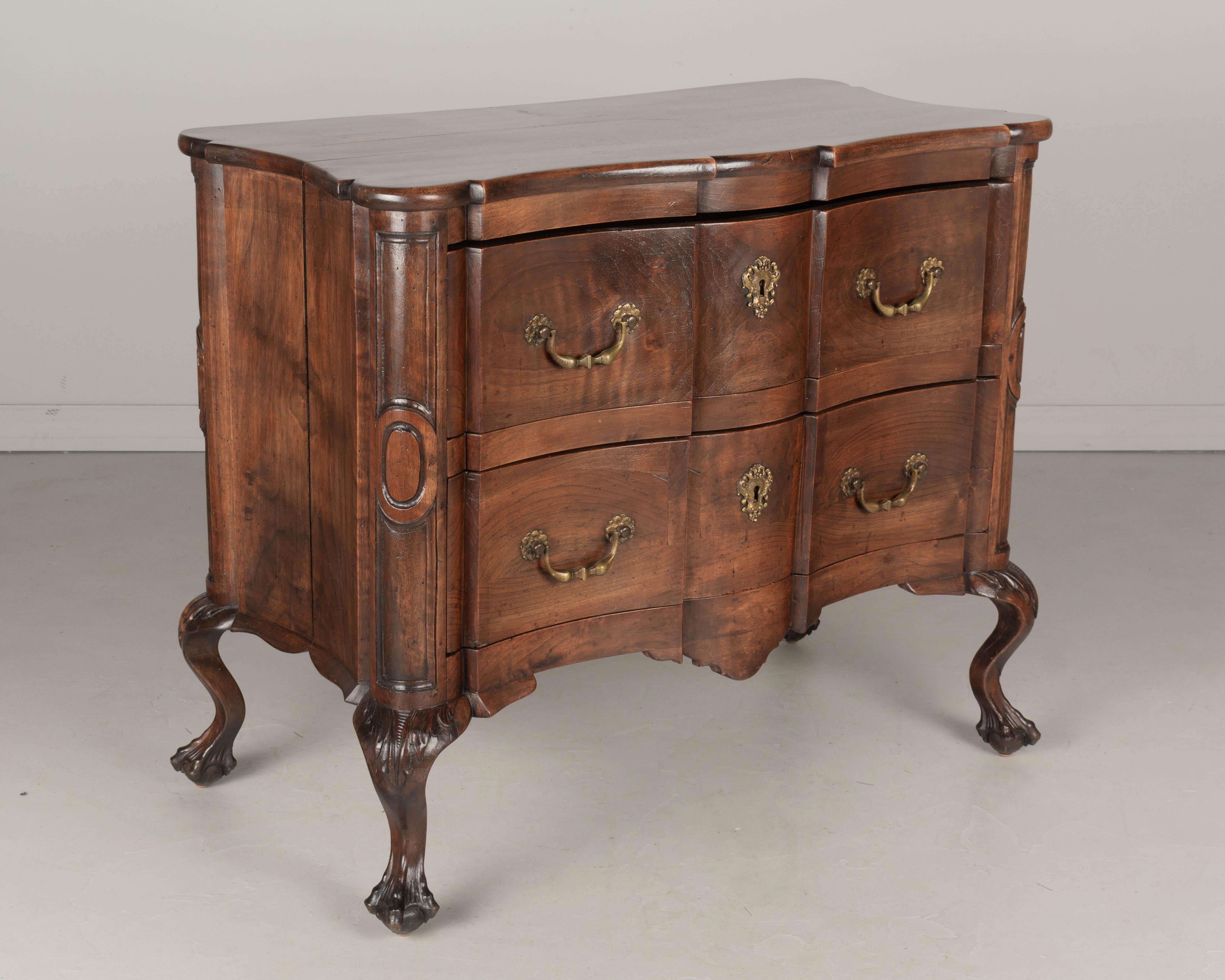 An early 19th century French commode made of solid walnut with an arbalète, or crossbow front and serpentine sides. Two deep dovetailed drawers with original bronze hardware. Locks are present, but no keys. Unusual short cabriole legs with carved