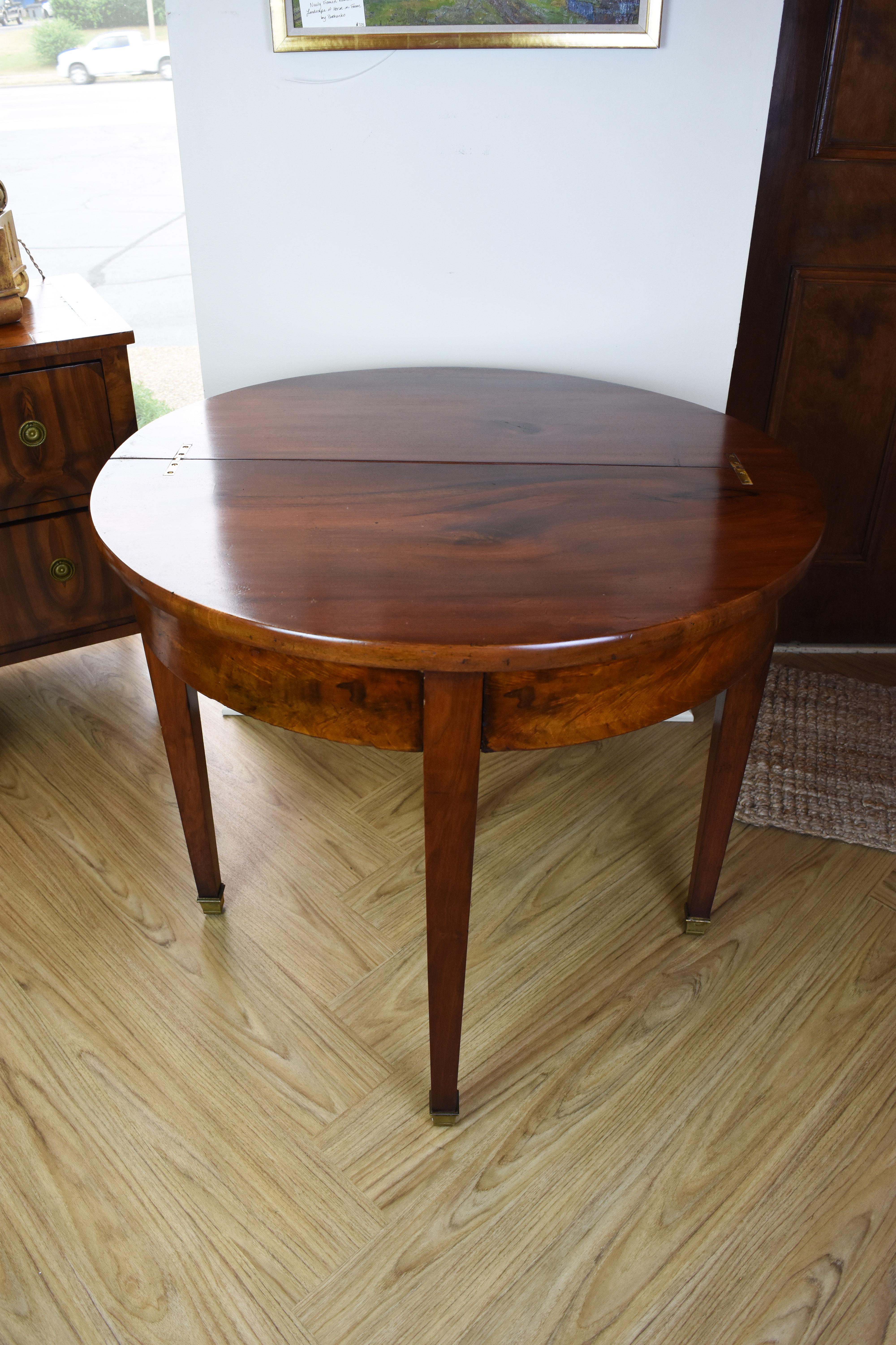 This French walnut demilune or console table features a beautiful, rich walnut finish and four tapered legs ending in brass cuffs. There is a hidden drawer on the back which pulls out to support the tabletop (along with the fourth leg) in the fully