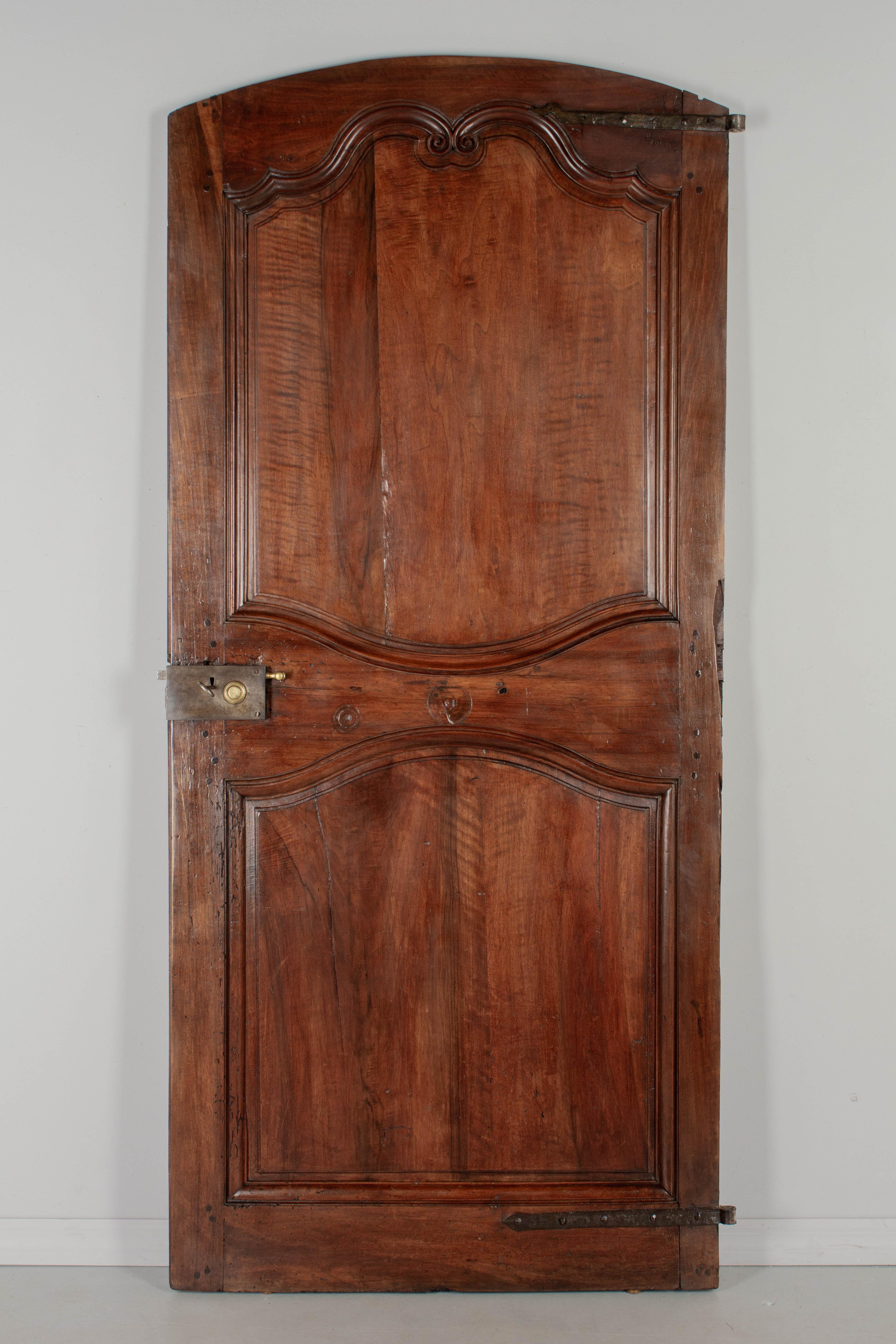 A 19th Century Louis XV style walnut door from the Loire Valley. This two sided interior door is made of thick planks of solid walnut with hand carved scroll decoration typical of the region. Large iron hinges. Working lock and key with brass knob