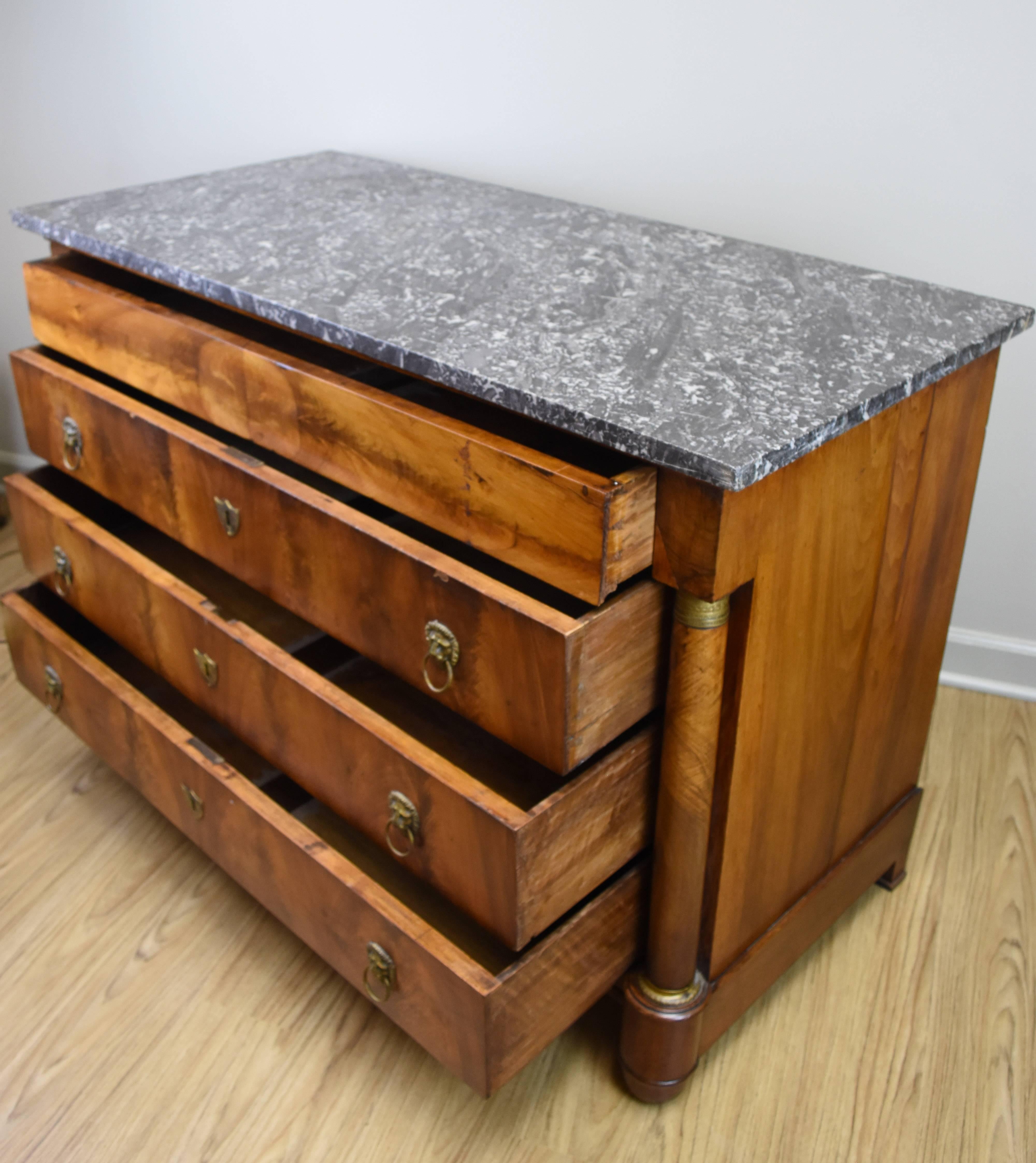 This French walnut Empire commode features a charcoal gray marble top and four functional drawers. The walnut veneer on the front is bookmatched and has a wonderful rich patina. Three of the drawers have pulls featuring a lions head motif and the