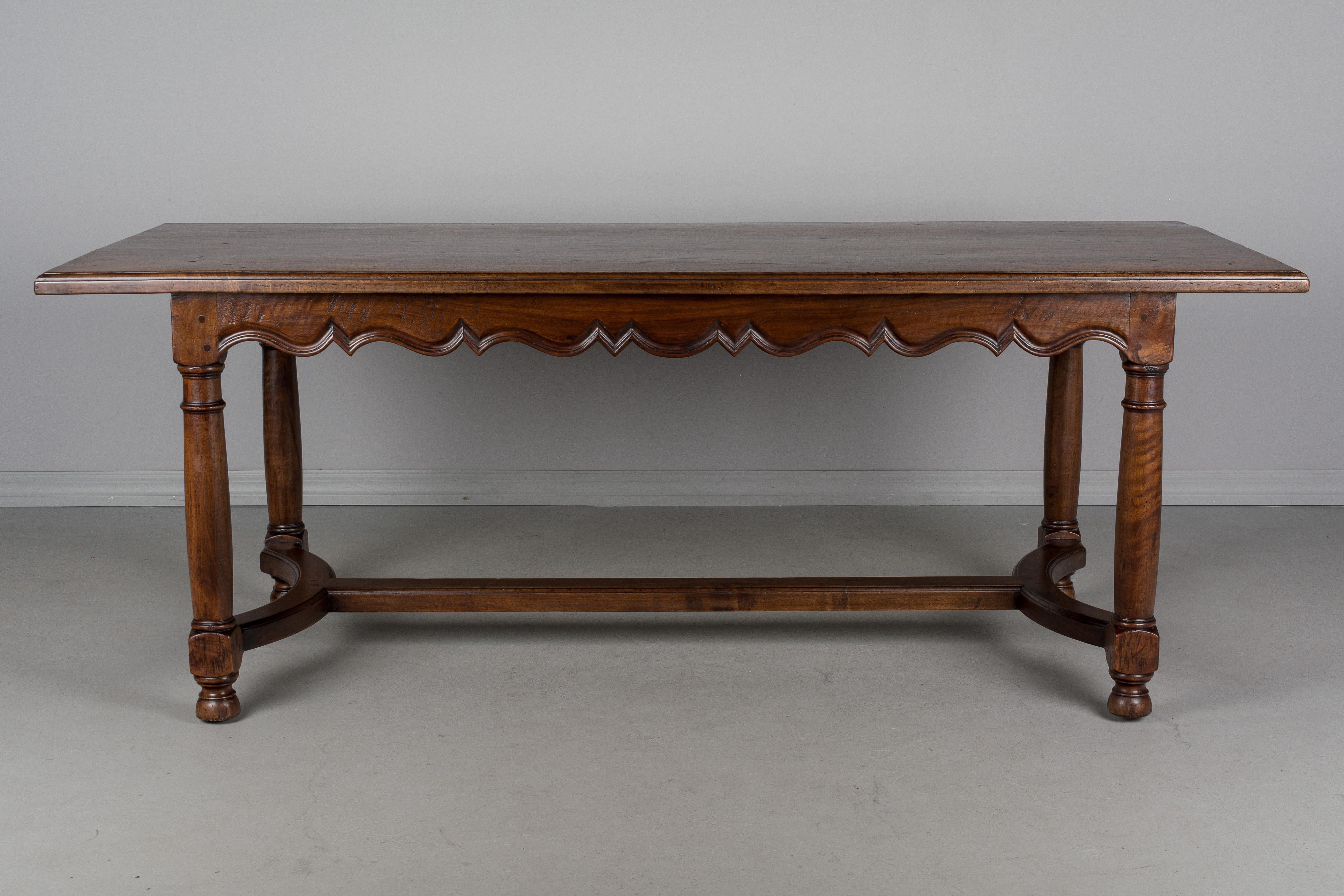 A beautiful French country farm table made of solid walnut with decorative scalloped apron, turned legs and a curved stretcher. A heavy, sturdy table of excellent quality, using pegged construction. The top is made of three planks of 1-1/4 inch