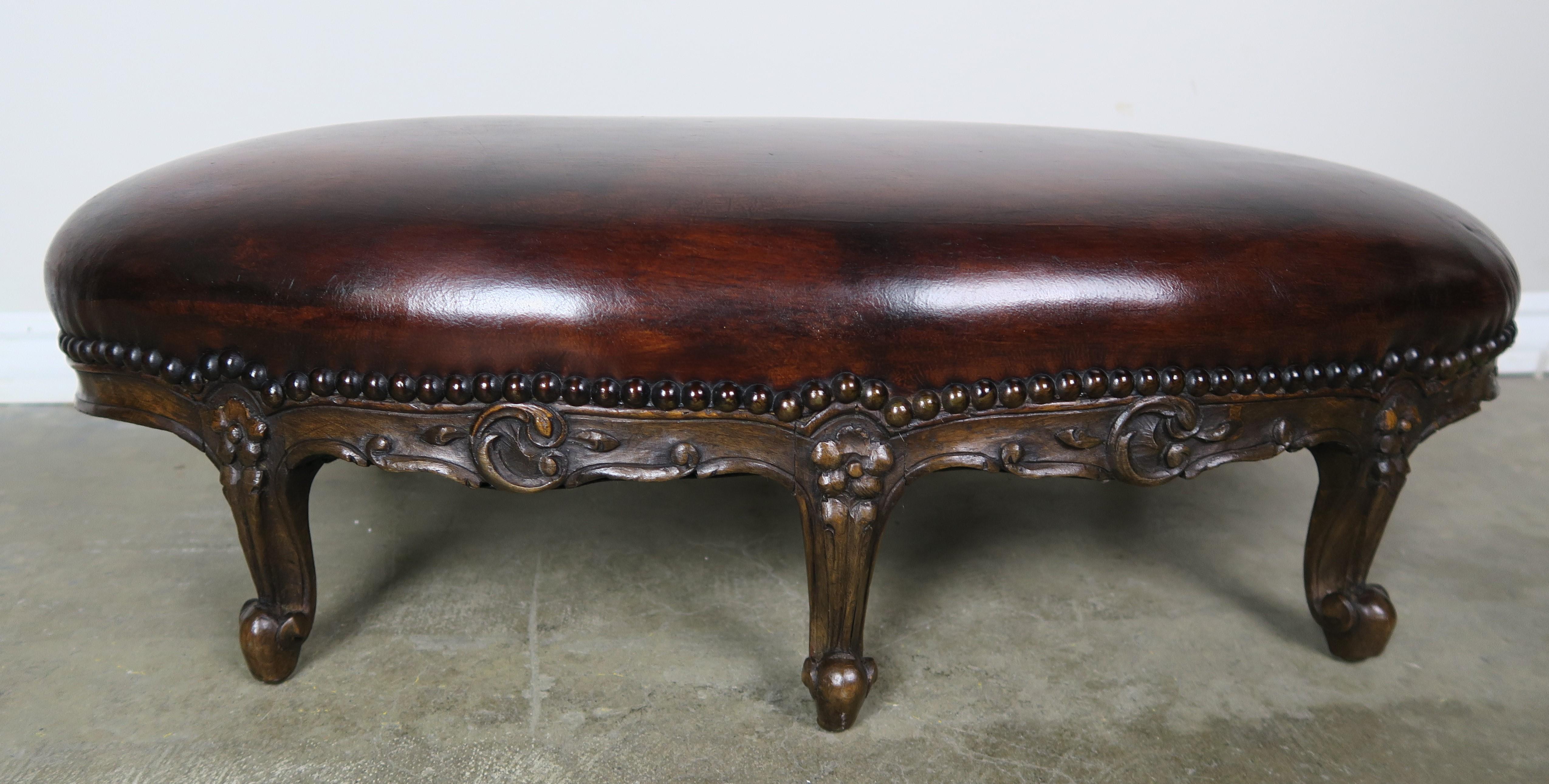 19th century French carved walnut six legged footstool in a Louis XV style frame standing on six cabriole legs that end in rams head feet. Beautiful patina on both frame and leather. The leather is detailed with antique brass colored nailheads.