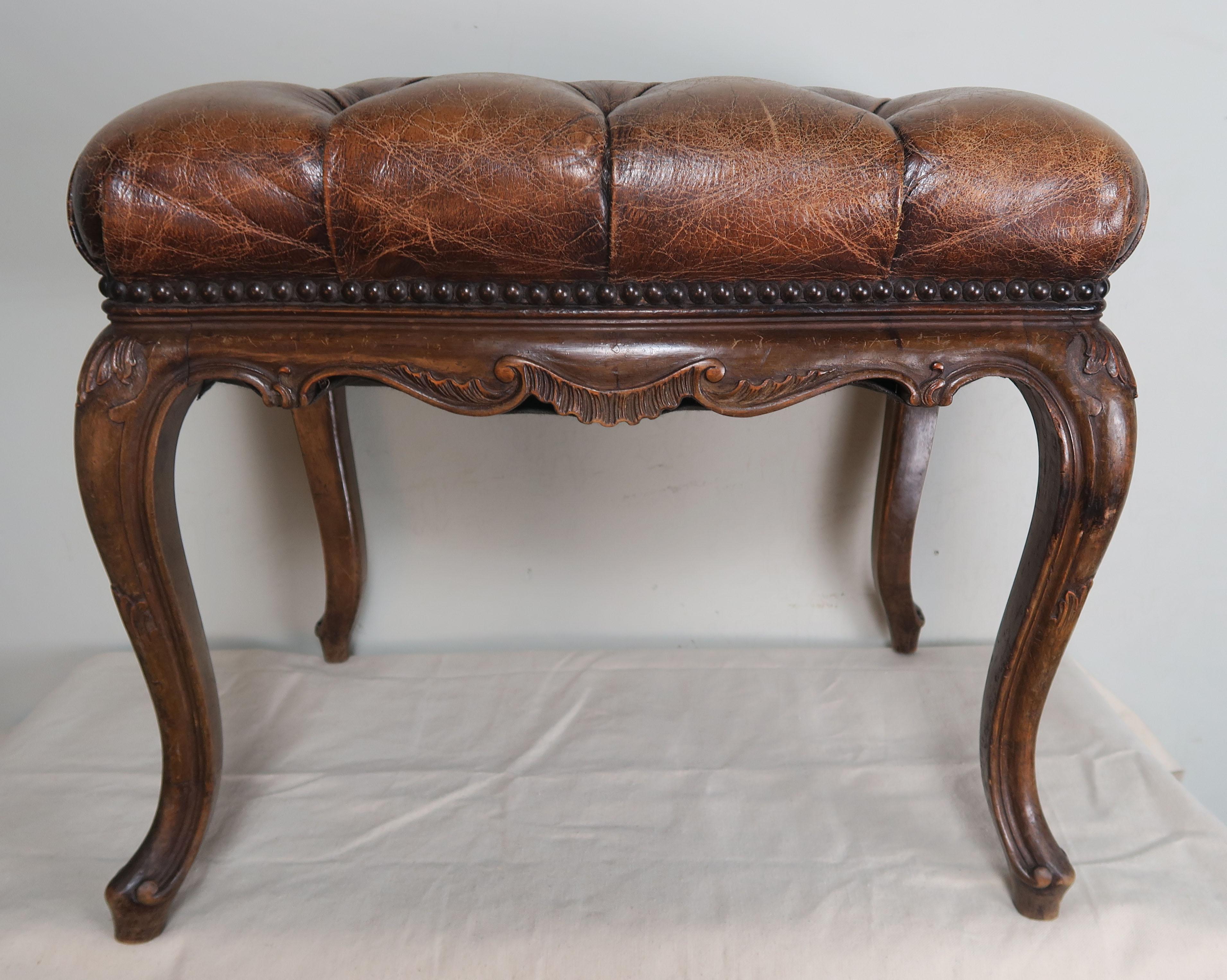 19th century French walnut bench that is upholstered in chestnut brown colored tufted leather with brass nailhead trim detail. The leather is beautifully worn. The bench stands on four cabriole legs that end in rams head feet.