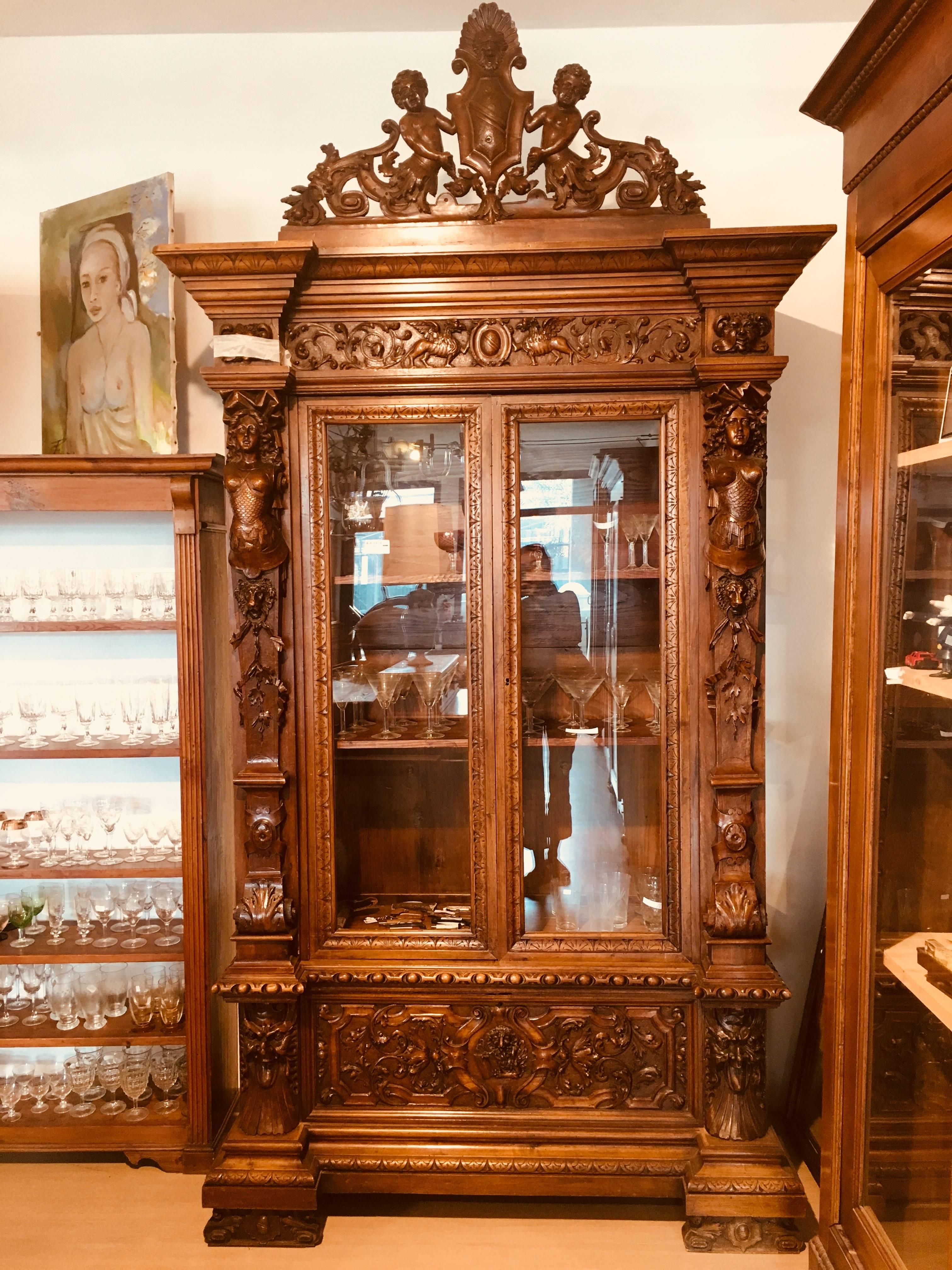 This magnificent and rare 19th century Renaissance grand cabinet with vitrines features intricate decorations heavily carved into the solid walnut wood. There are massive carved wood columns with women's bodies in the centre. This beautiful piece is