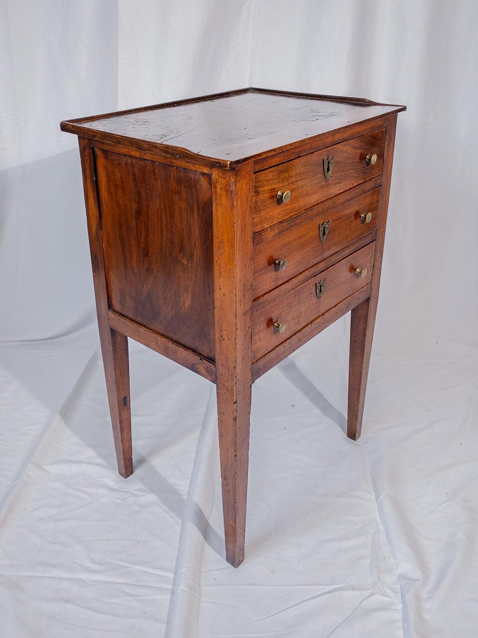 This elegant 19th-century French side table exudes timeless charm with its rich walnut wood and intricate craftsmanship. Standing gracefully on slender legs, it features three spacious drawers adorned with delicate brass handles, offering both