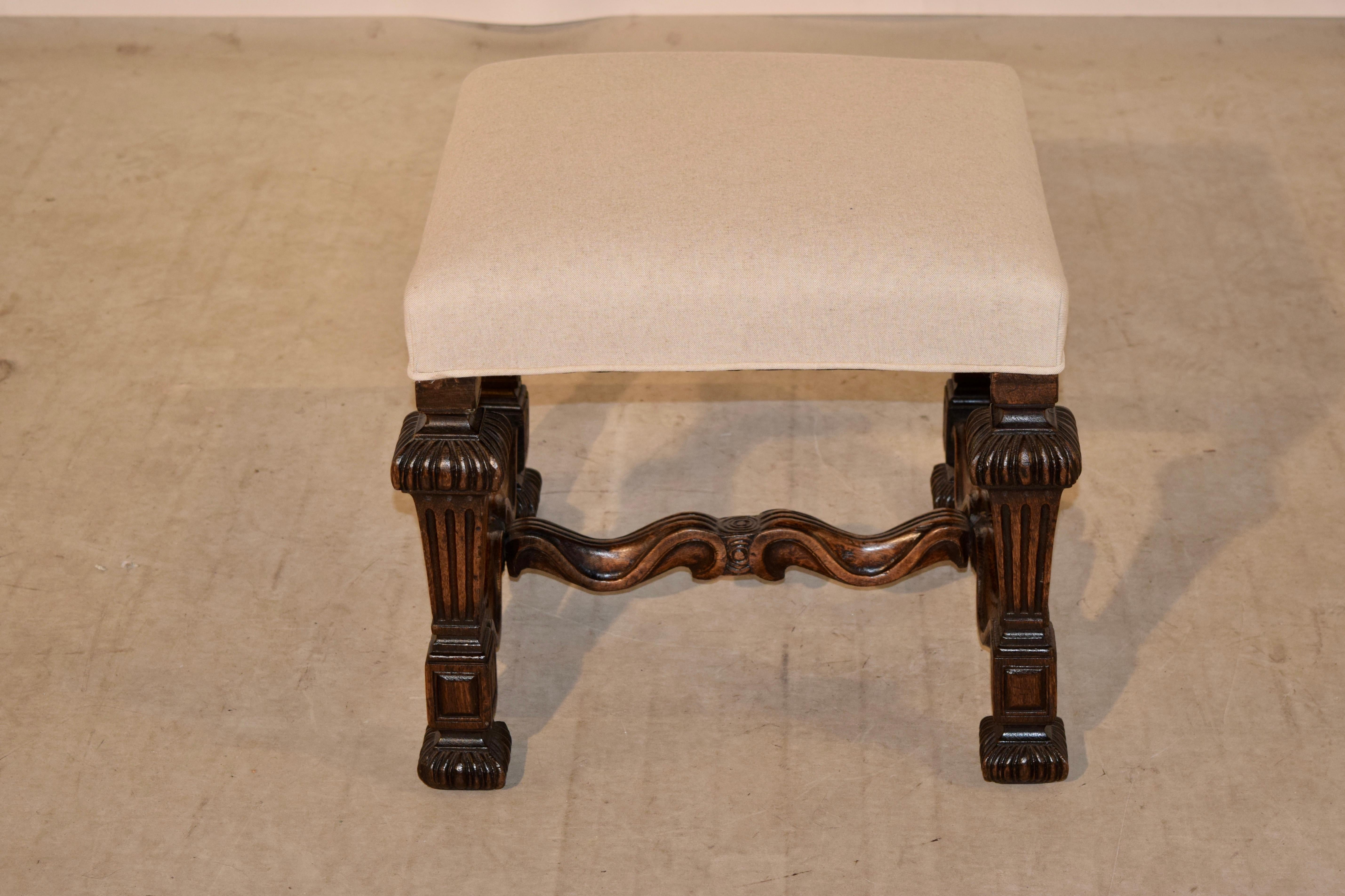 19th century walnut stool from France with a newly upholstered top in linen. The legs are highly carved in a reeded and fluted patterns, joined by scalloped and shaped stretchers.