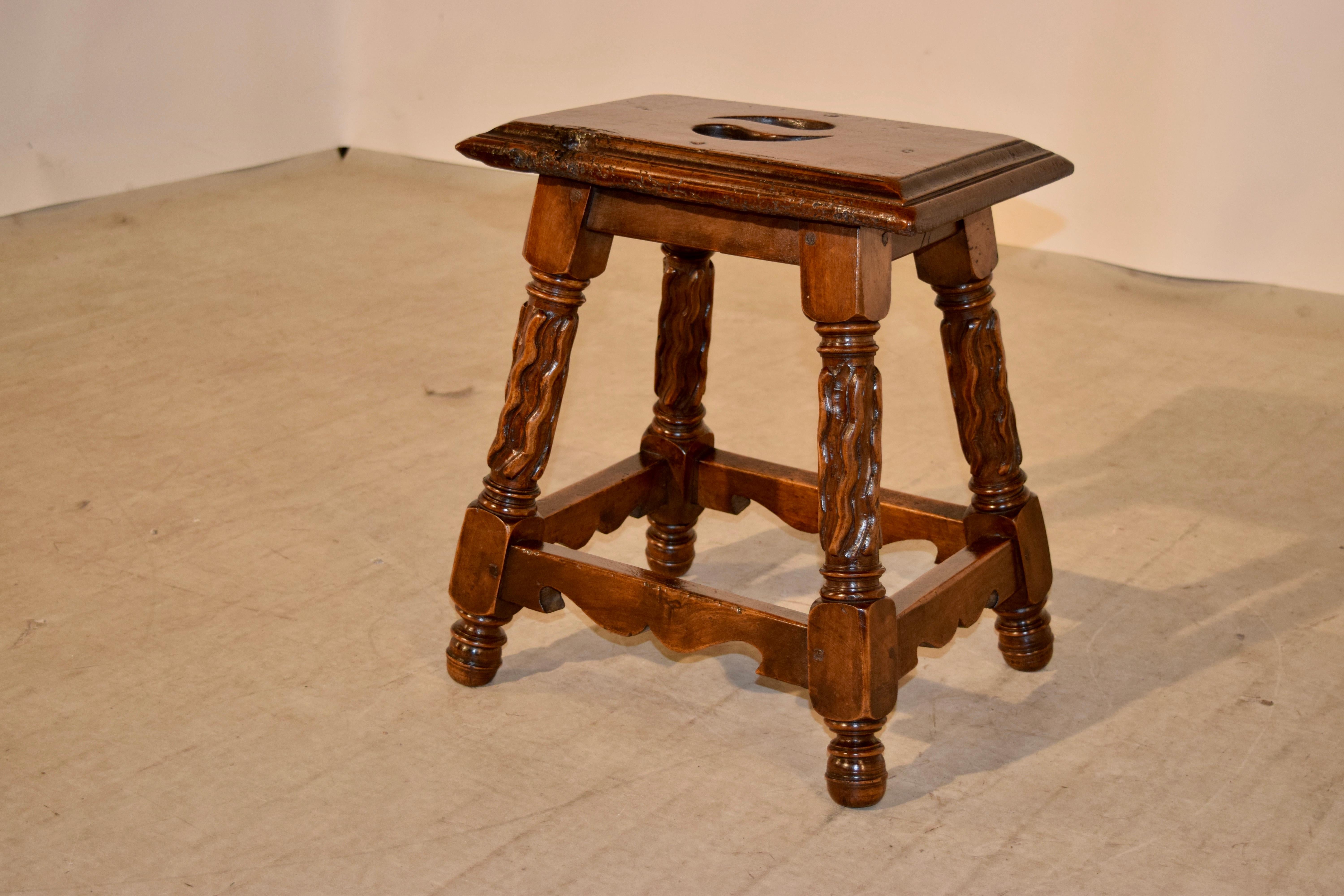 19th century French stool made of walnut. The top has a wonderfully bevelled edge, with an original knot included in the top which has a nice burl quality. The apron is simple and follows down to splayed legs which are hand-carved and decorated in