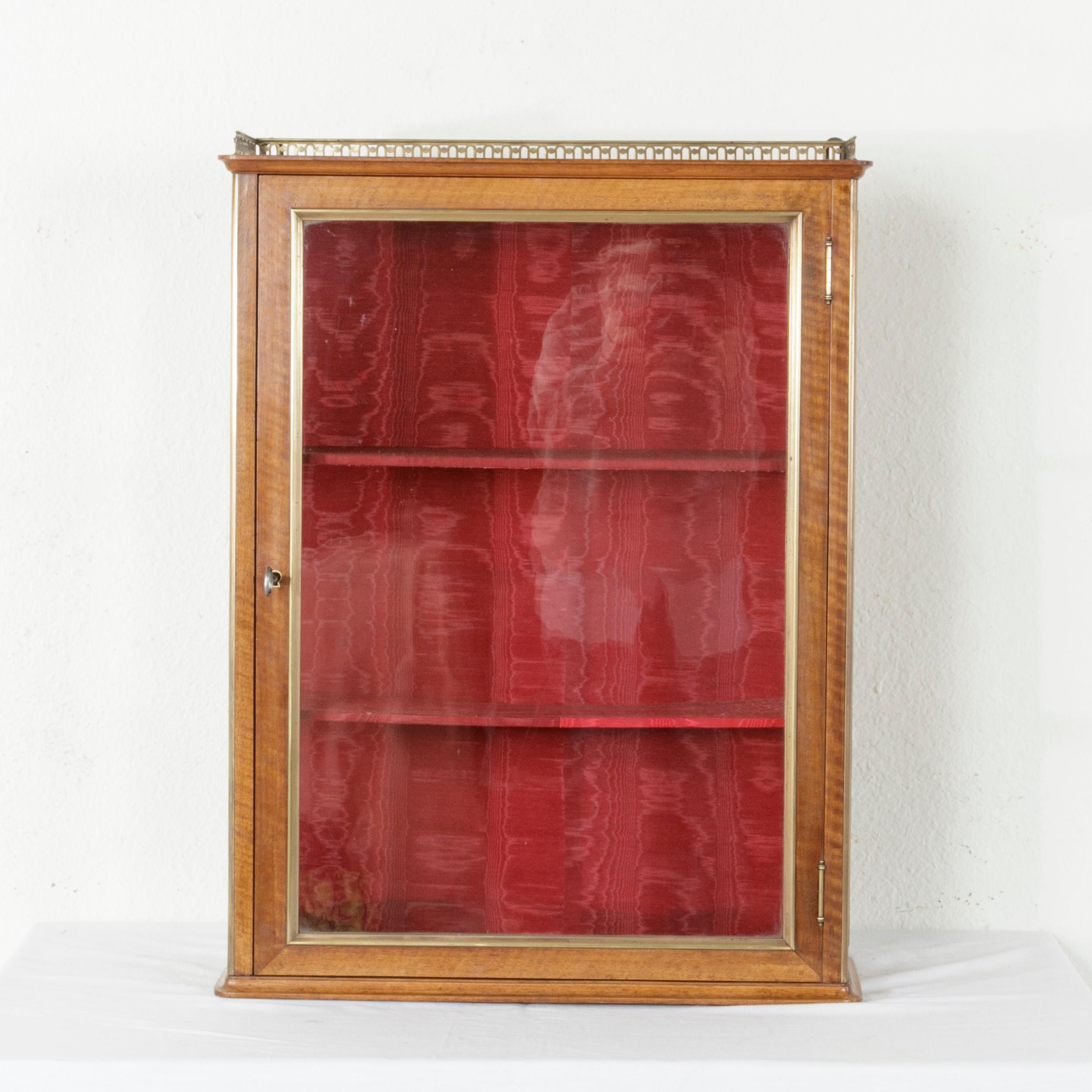 This late 19th century French tabletop walnut vitrine or display cabinet features bronze trim around its hand blown glass door and sides as well as a bronze gallery on the top. The interior is fitted with two shelves and is lined with red moire